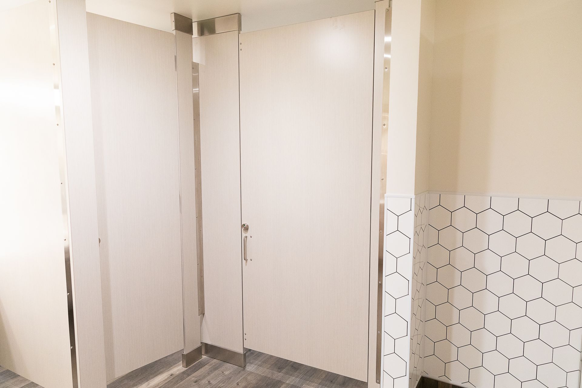 Empty public restroom with beige stalls and white tiled wall.