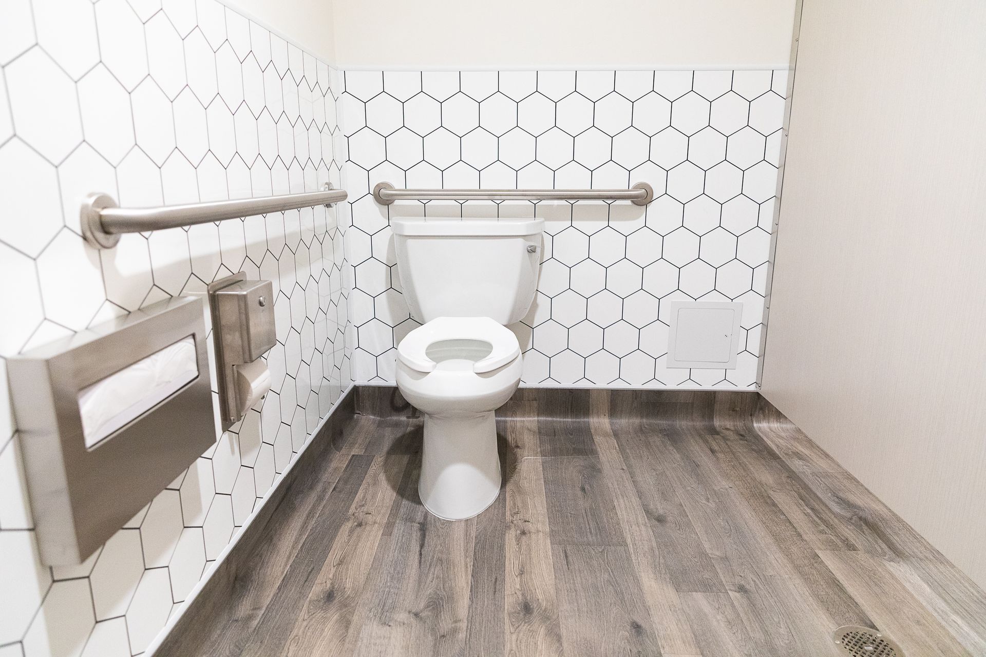 Accessible restroom with toilet, grab bars, toilet paper holder, and wood-look flooring