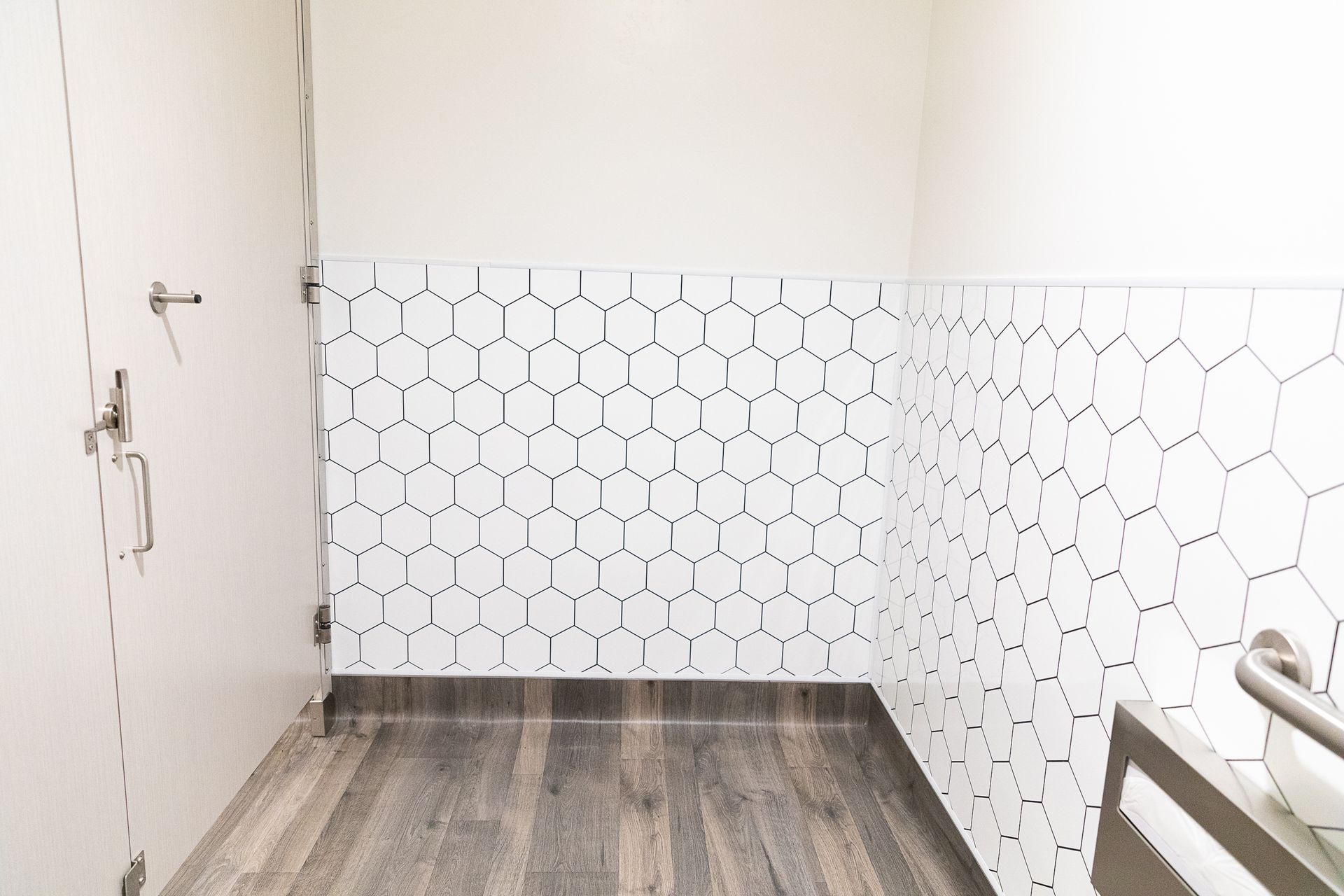Empty tiled bathroom with white walls and gray wood-look floor, no fixtures visible