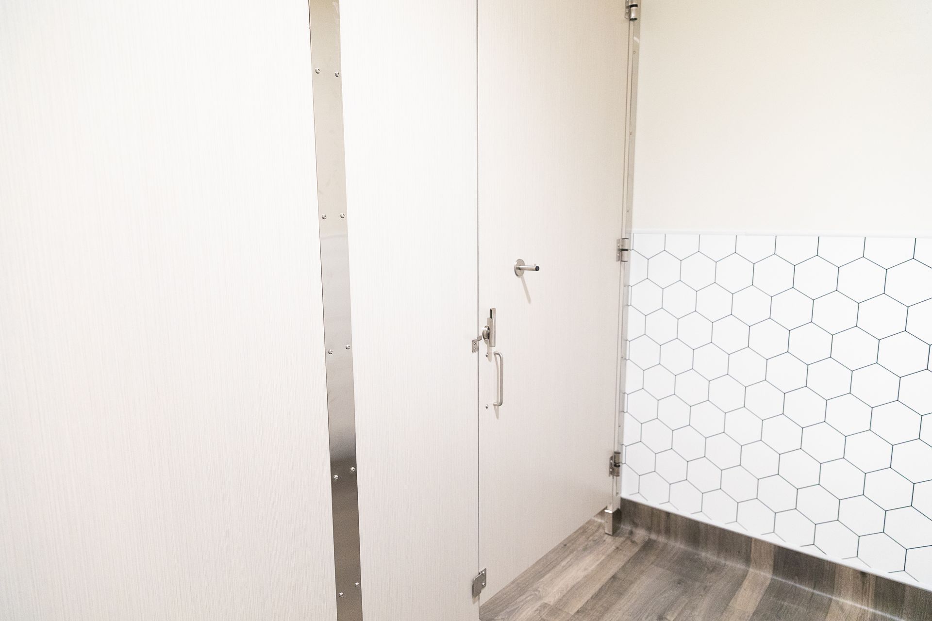 White hallway with a closed door, hexagon tile accent wall, and wood-look flooring.