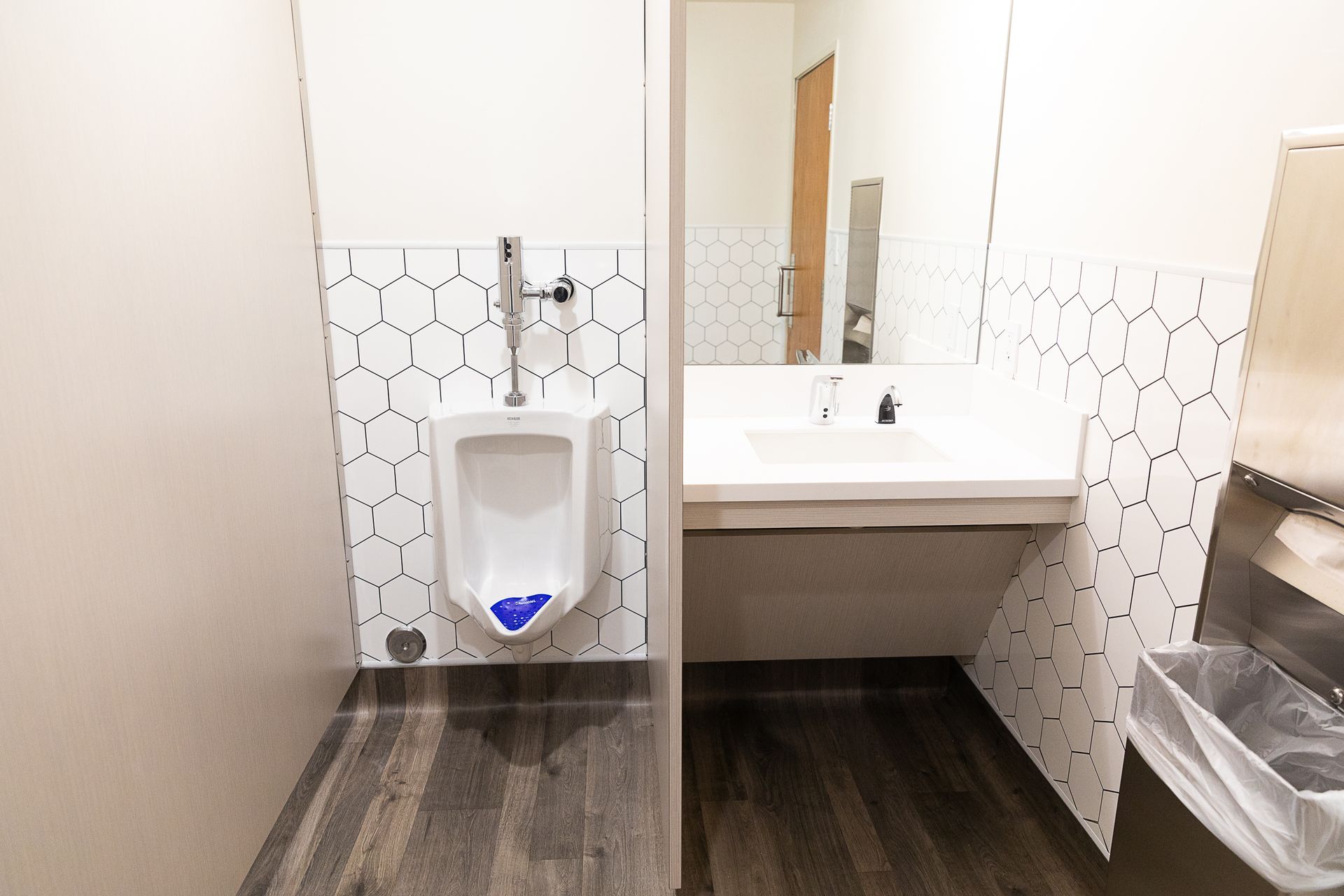 Public restroom with wall-mounted urinal, sink, and hexagonal tile backsplash