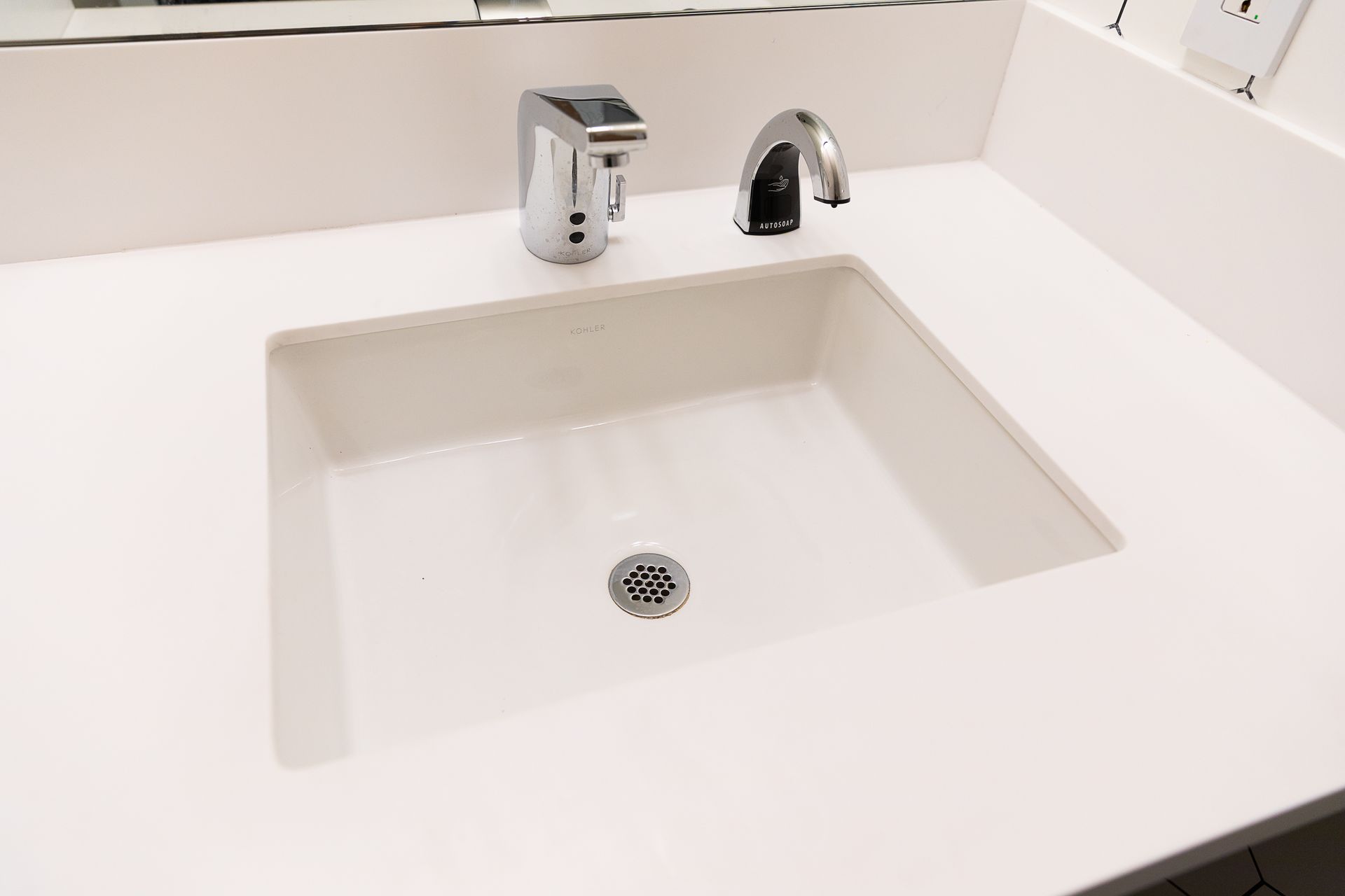 Modern white bathroom sink with chrome faucet and soap dispenser on a white countertop