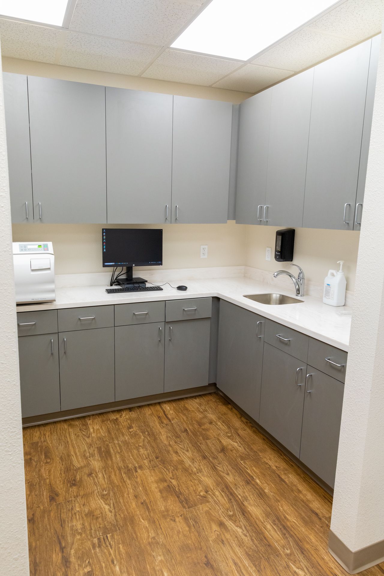 A kitchen with gray cabinets , a sink , and a computer on the counter.