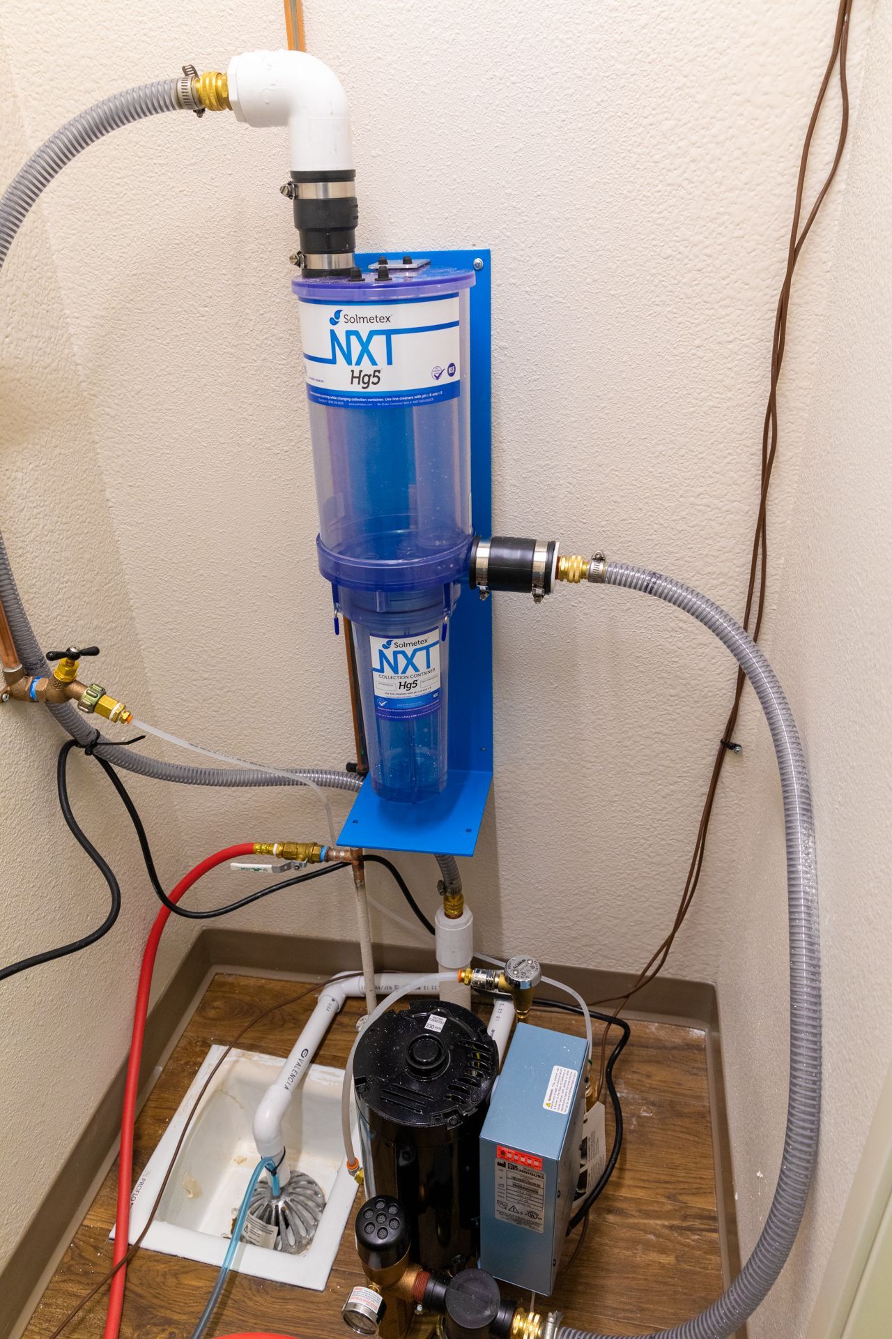 A water filter is sitting on a wooden floor next to a wall.