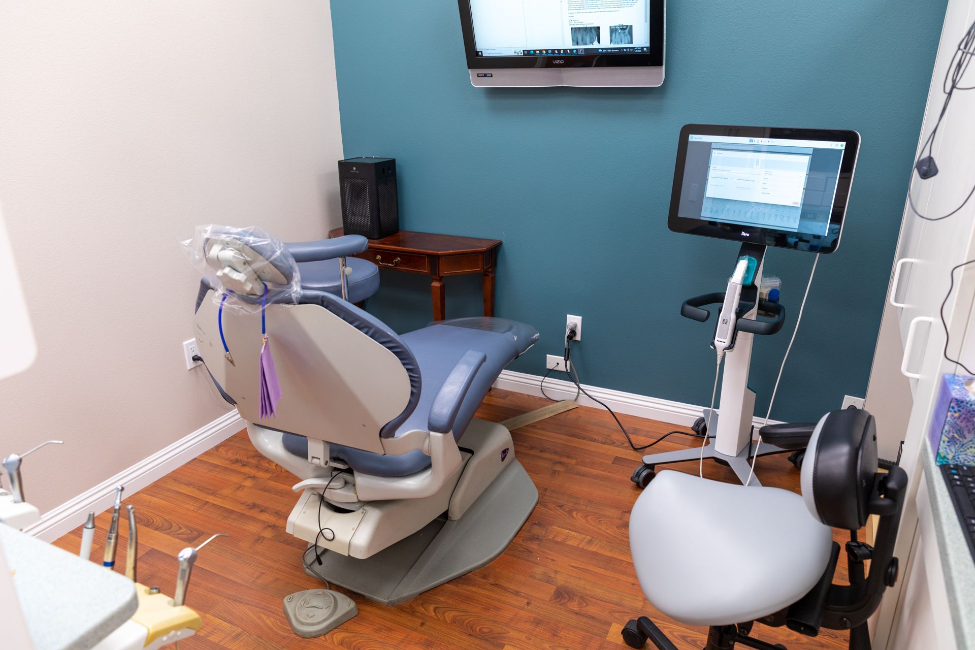 A dental office with a dental chair and a monitor on the wall.