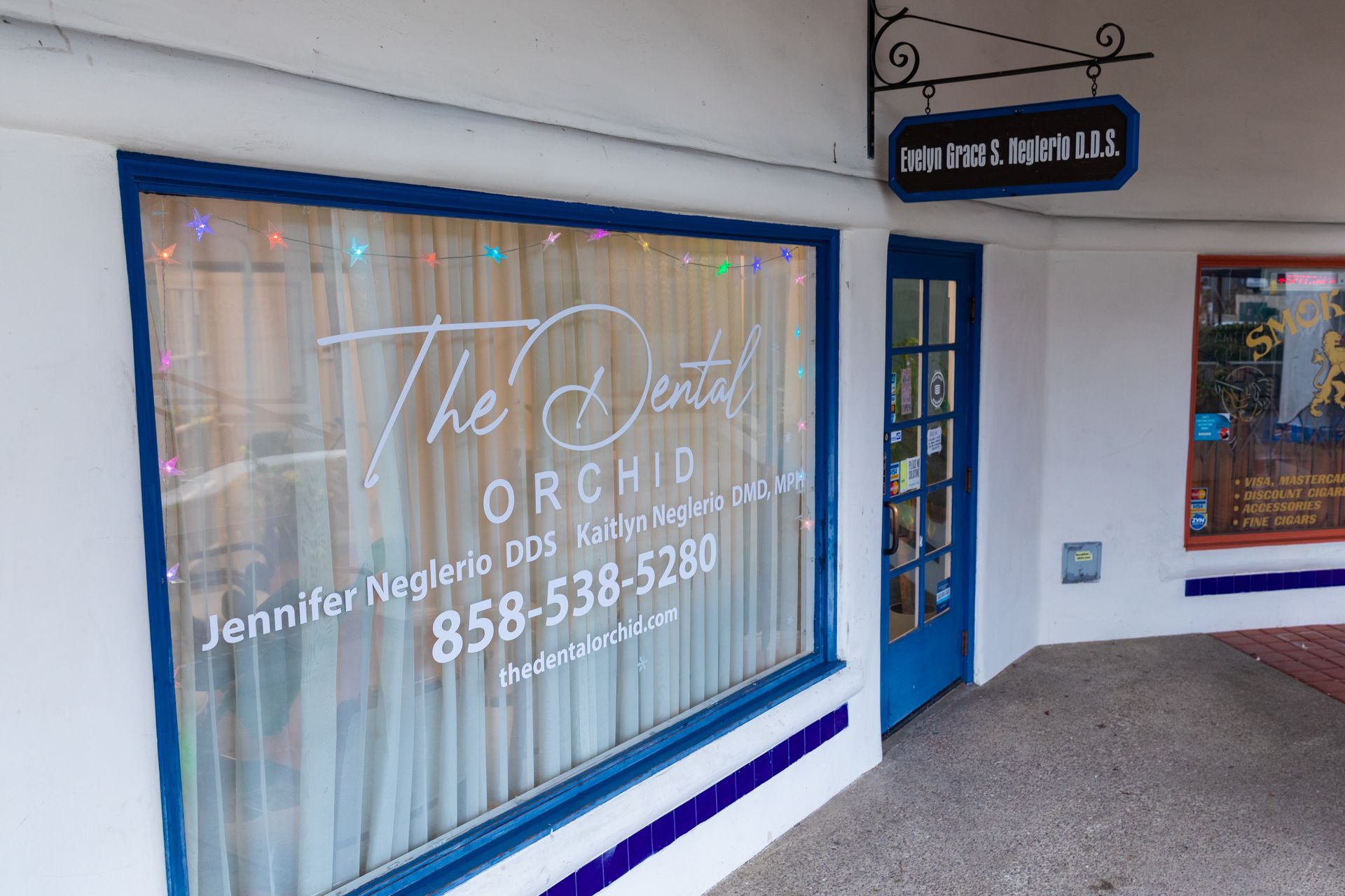 A white building with a blue door and a window with the words `` the dental orchid '' written on it.