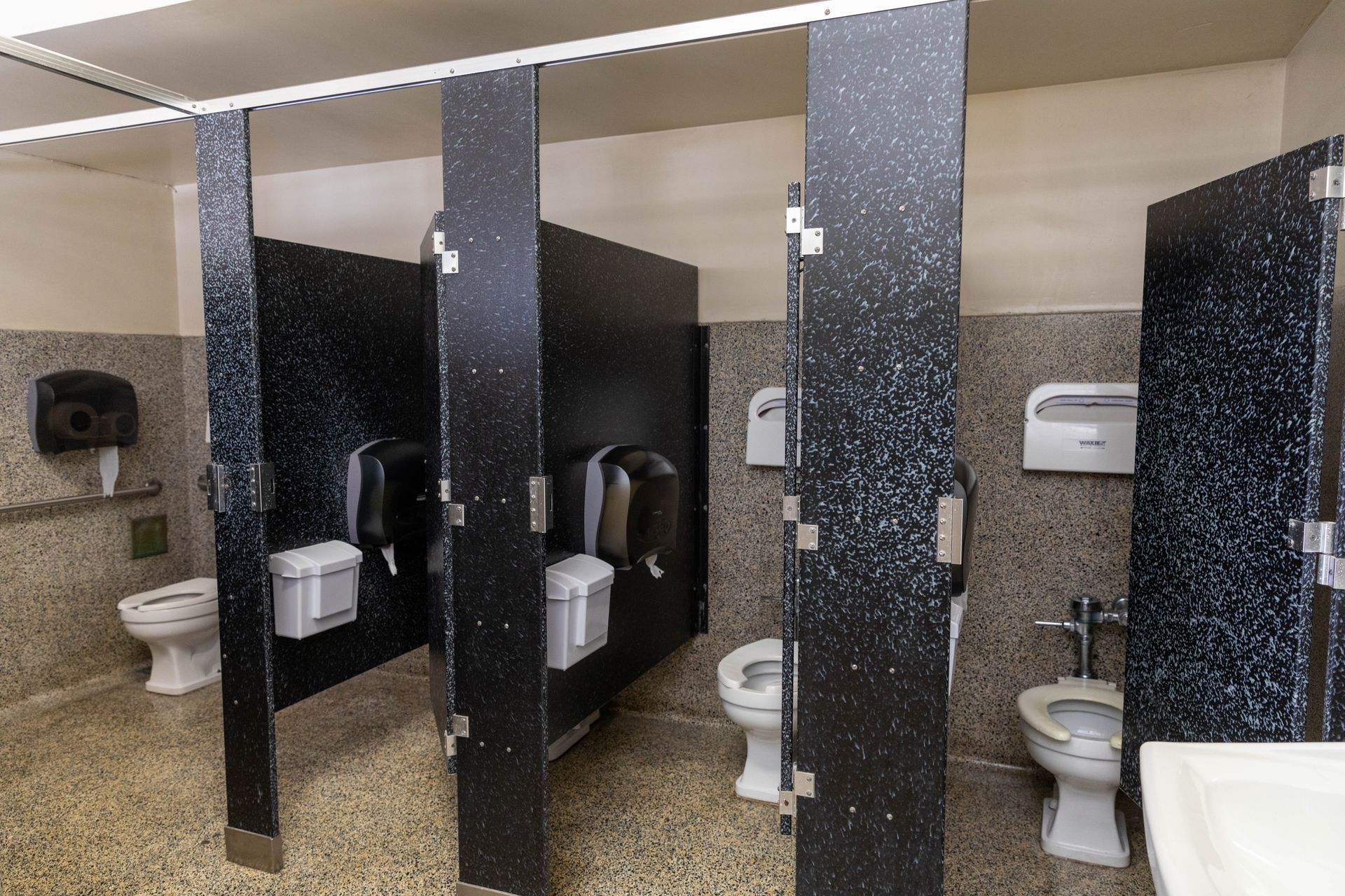 A public restroom with black dividers and toilets