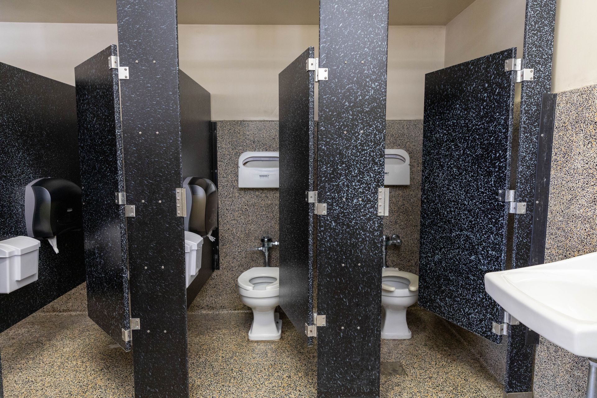 A public restroom with three toilets and a sink