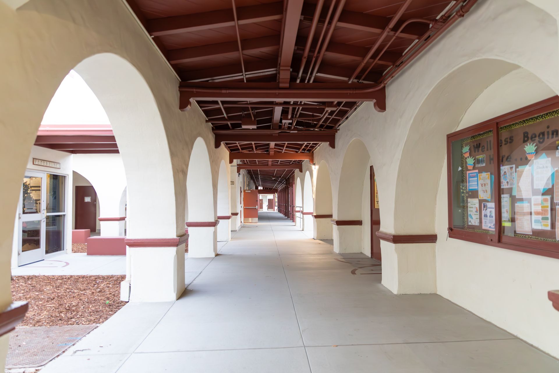 An empty hallway with arches and bulletin boards in a building.