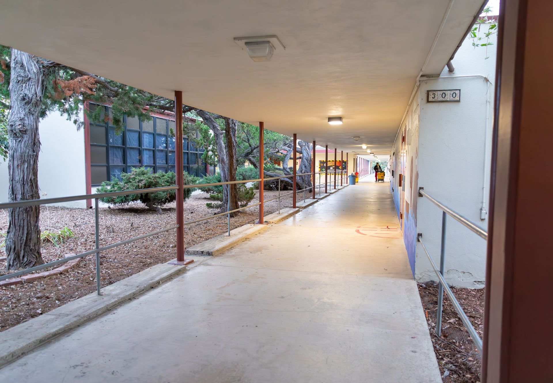 A long covered walkway between two buildings with trees in the background.