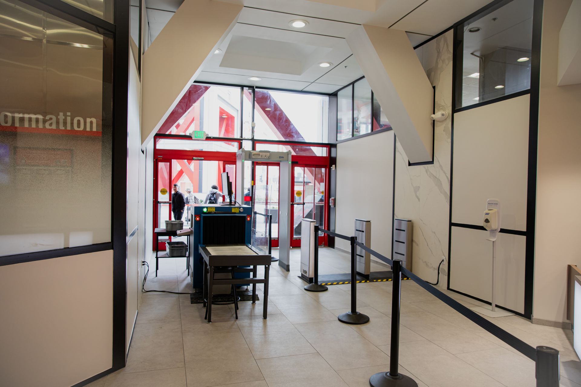 Airport security checkpoint with red metal detectors, a screening table, and roped queue area.