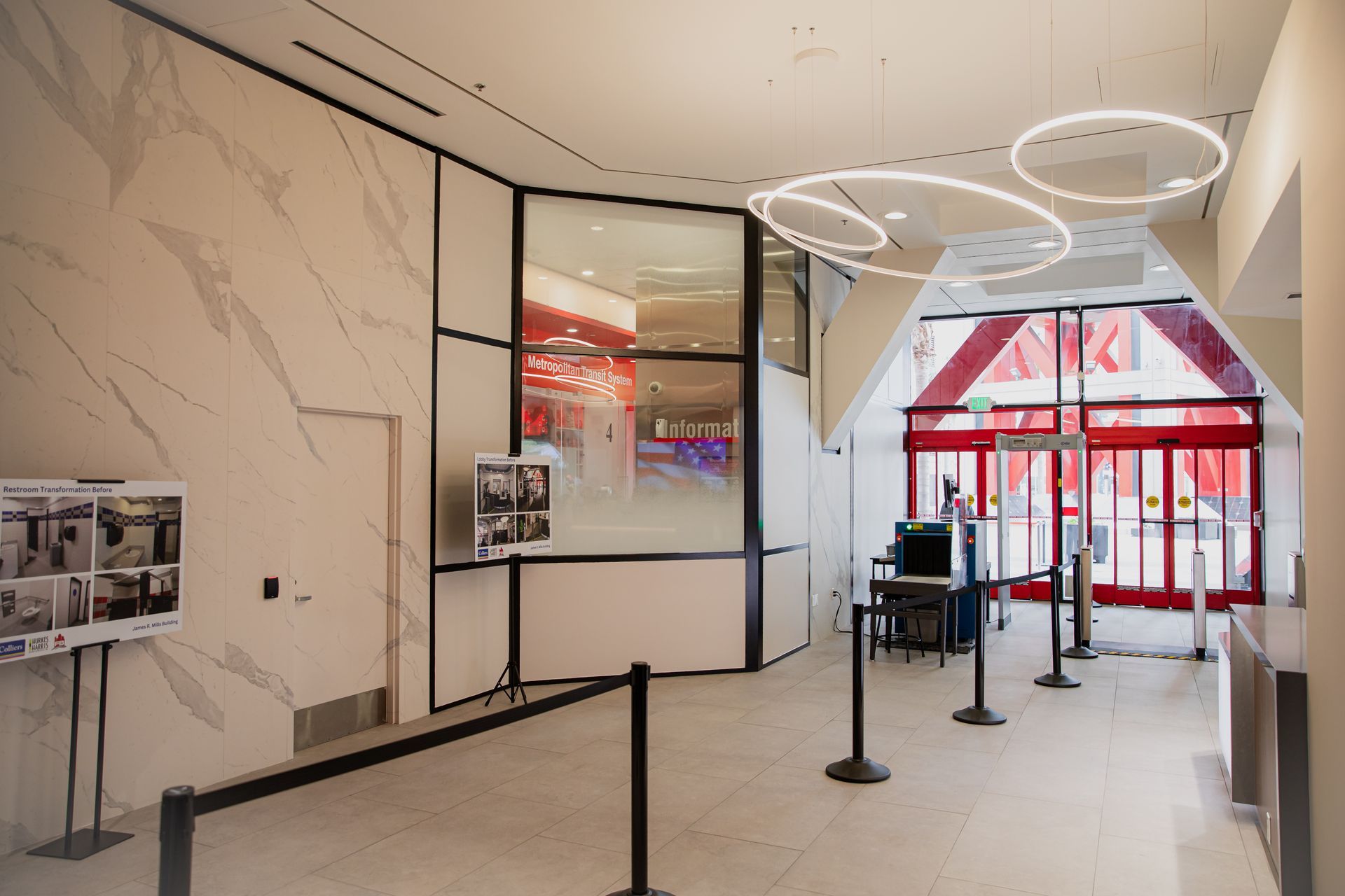 Empty airport lobby with marble walls, black stanchions, and red automatic doors