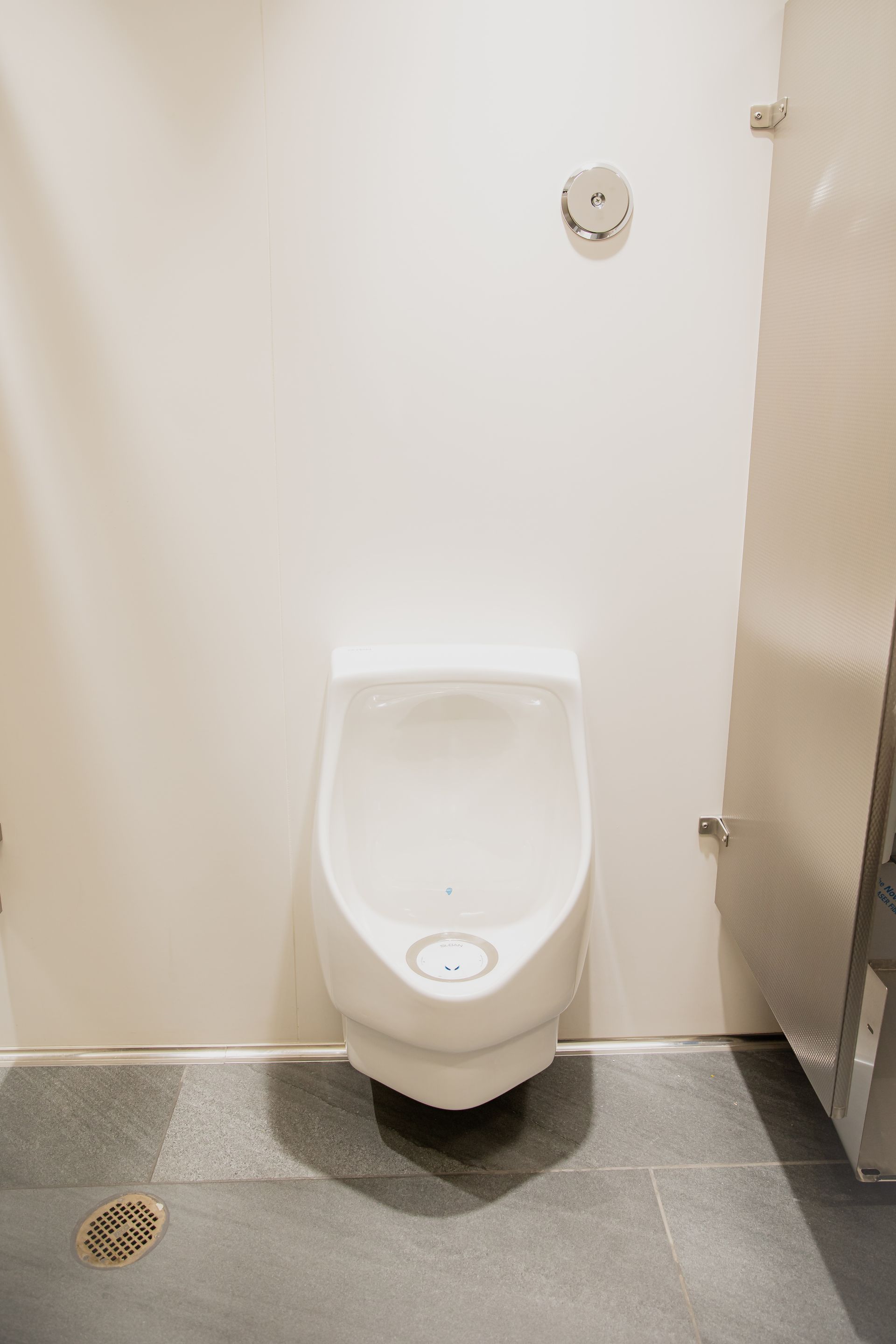 Public restroom toilet stall with a white urinal-like fixture, gray floor, and stall divider.