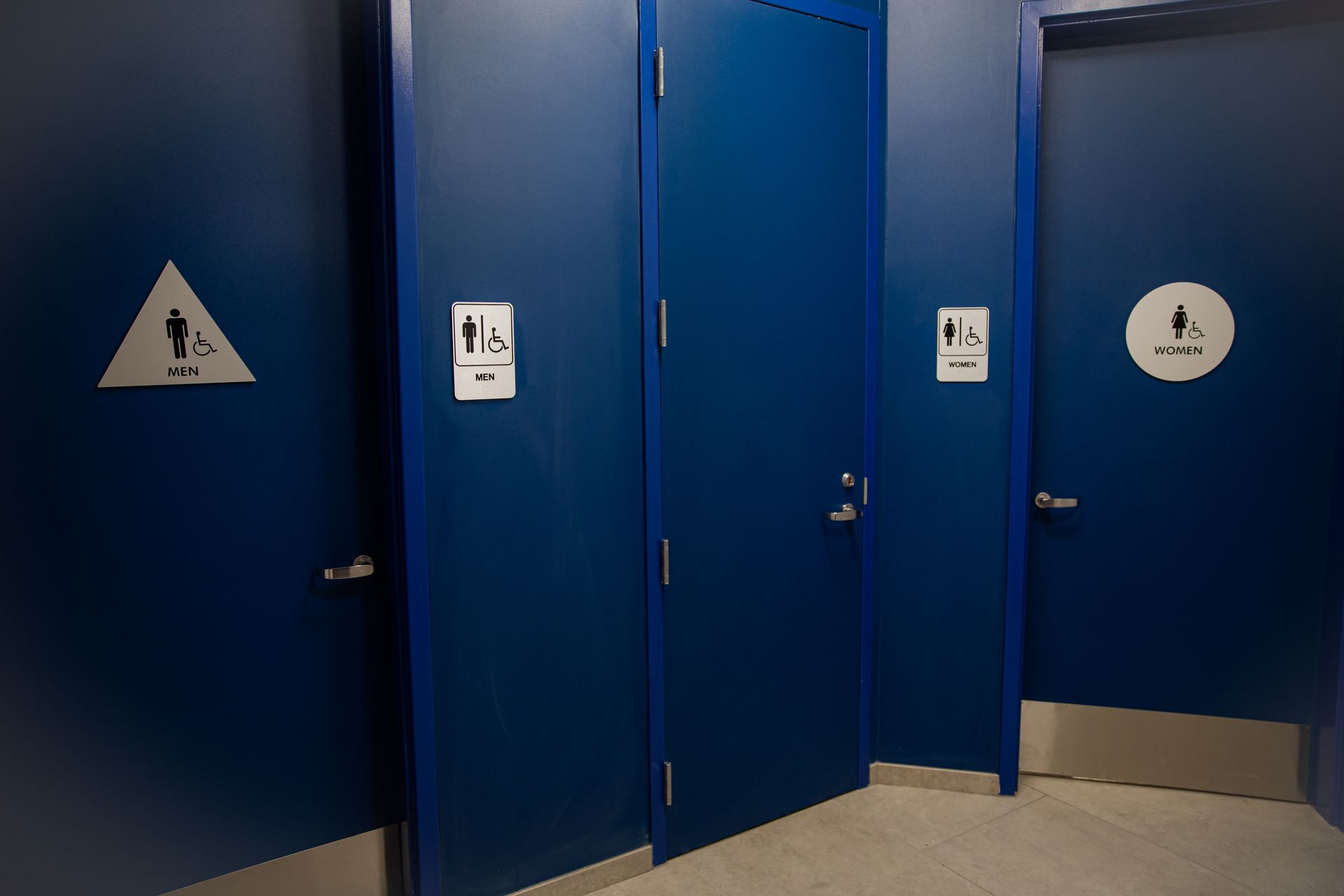 Blue restroom doors in a hallway, with gender and accessibility signs above the stalls