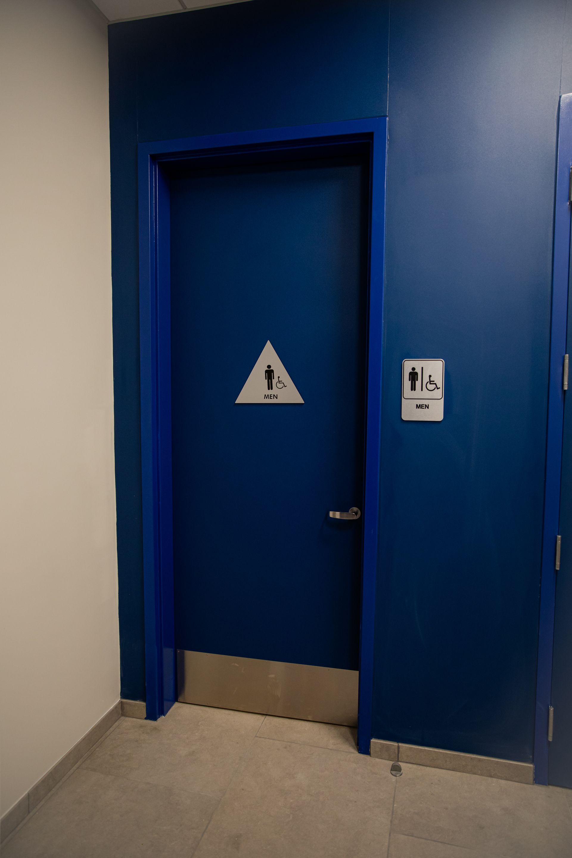 Blue restroom door with handicap sign in a hallway, next to an accessible stall door
