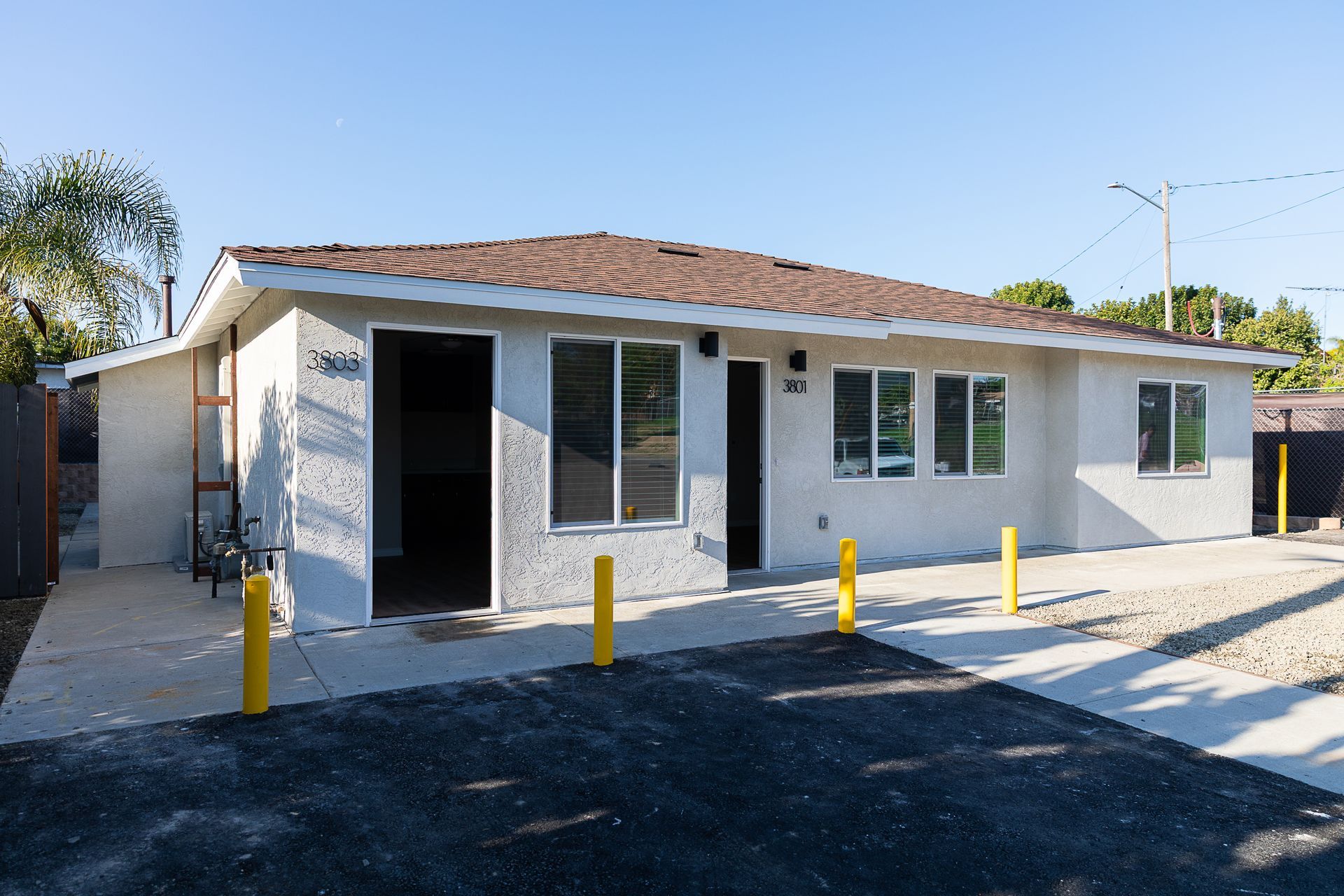 Single-story house with white exterior, tiled roof, and yellow bollards along the front drive.