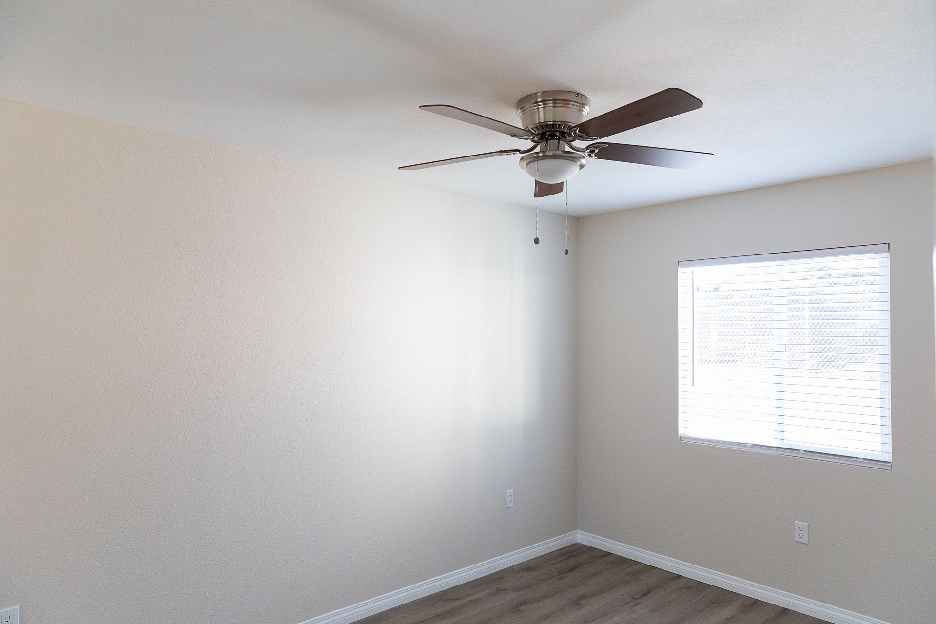 Empty white bedroom with a ceiling fan, window blinds, and wood-look flooring.