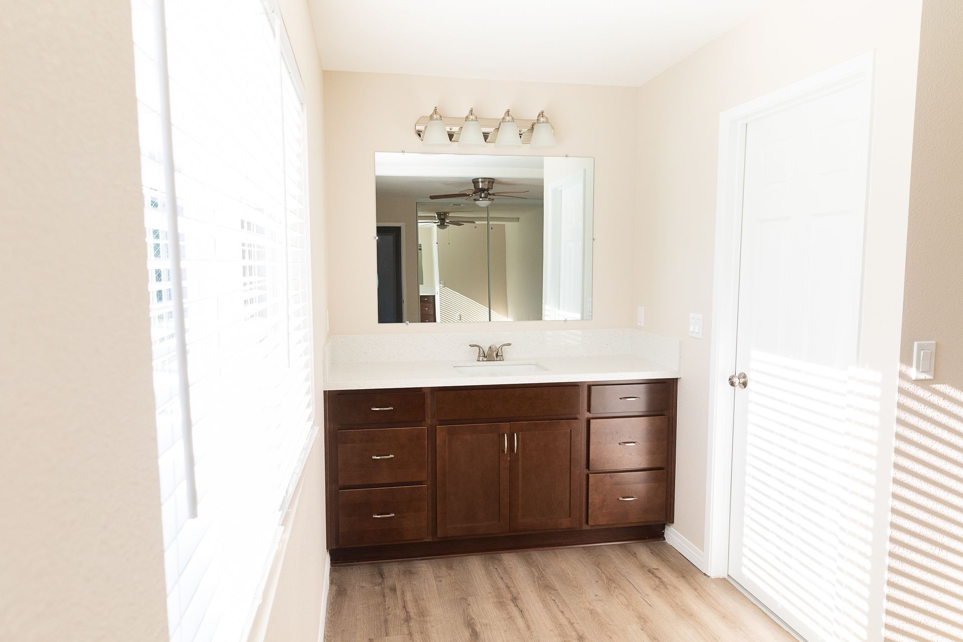 Bright bathroom with dark wood vanity, large mirror, white walls, and louvered doors on the right