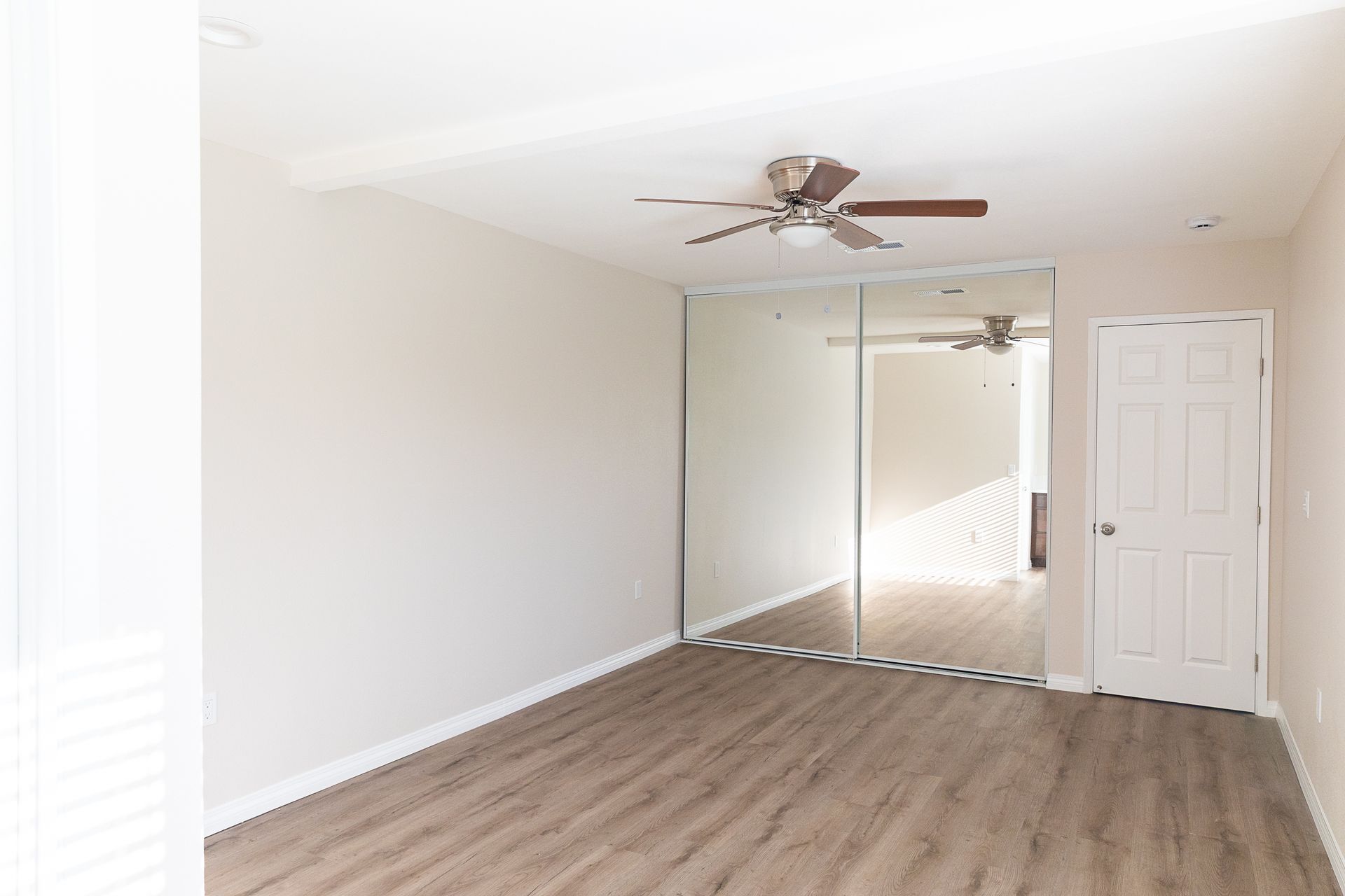 An empty room with a ceiling fan and a large mirror.