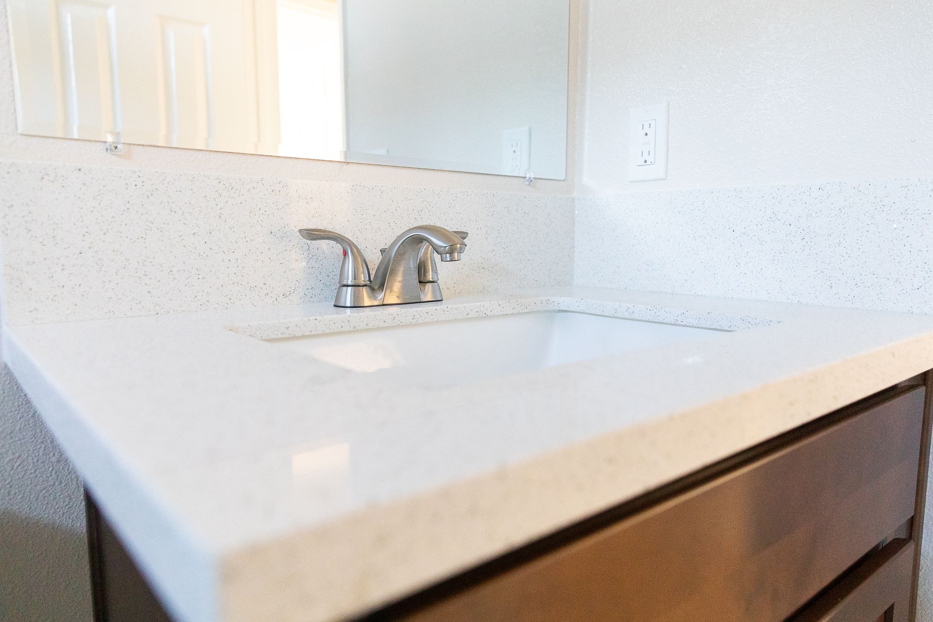White bathroom vanity with sink, chrome faucet, and mirror above a dark wood cabinet