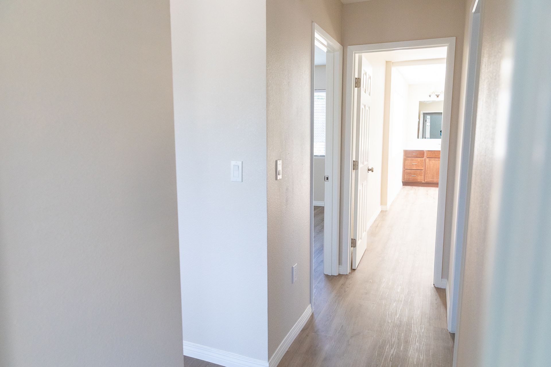 A hallway in a house with hardwood floors and a bathroom.