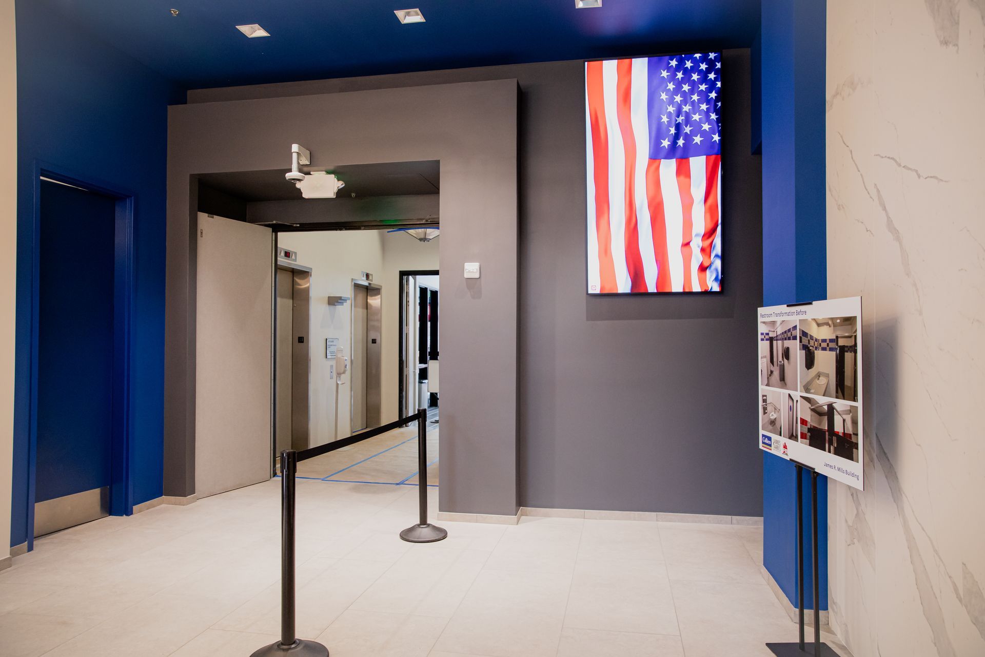 Airport hallway with a large U.S. flag display and stanchions guiding a walkway