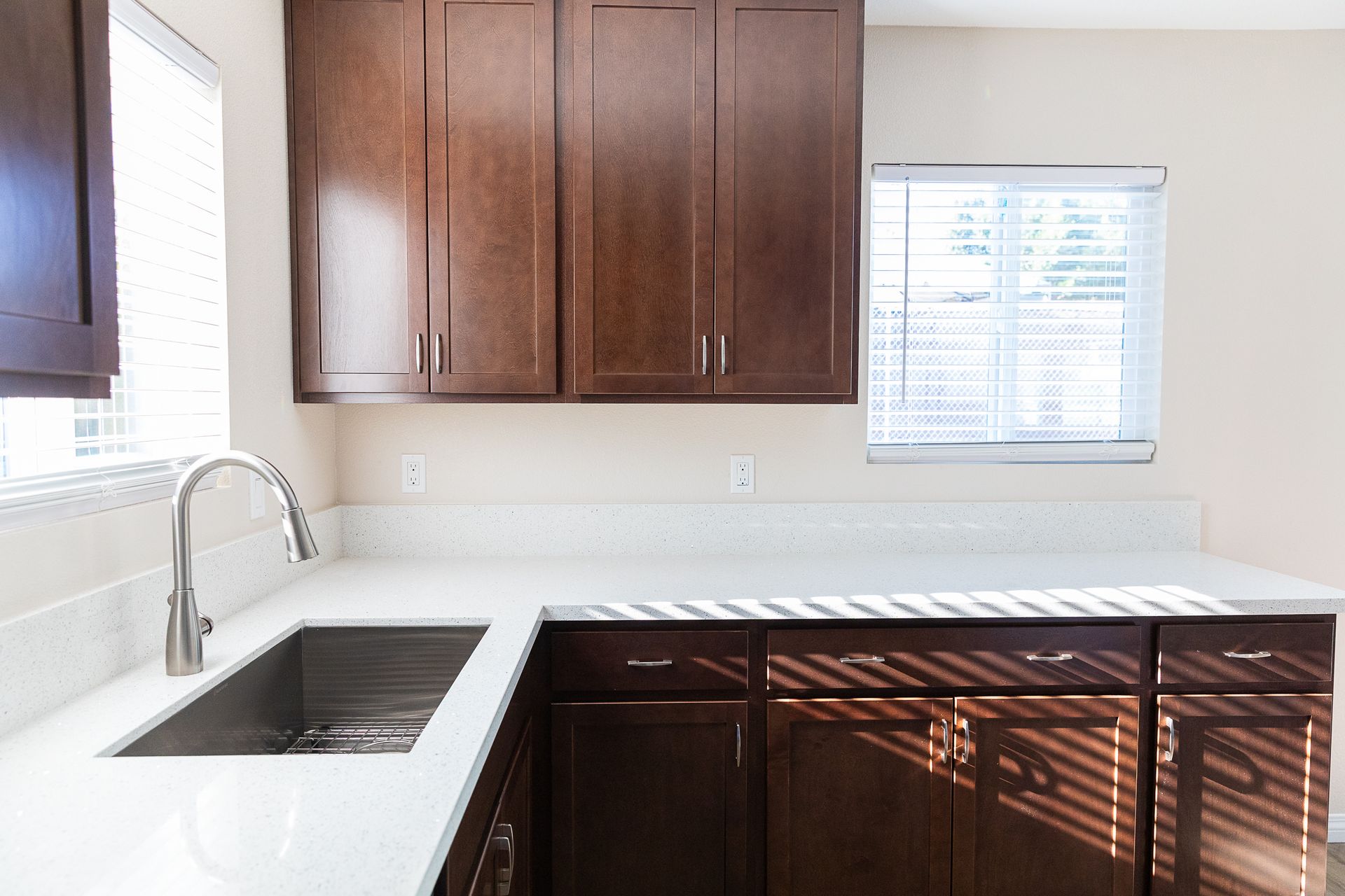 Bright kitchen with dark wood cabinets, white countertops, sink, and window blinds