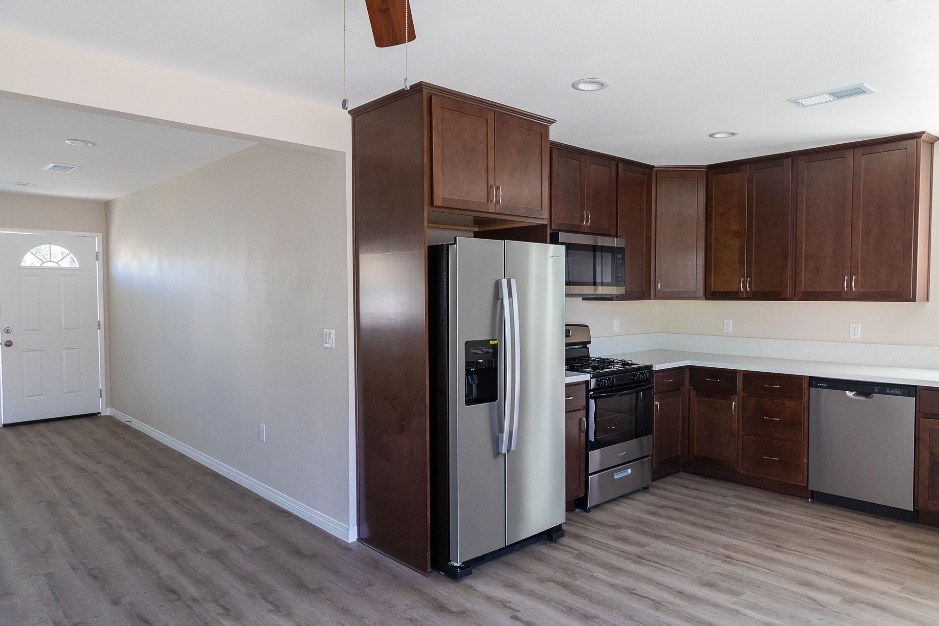 Open kitchen with dark wood cabinets, stainless steel appliances, and light wood flooring.