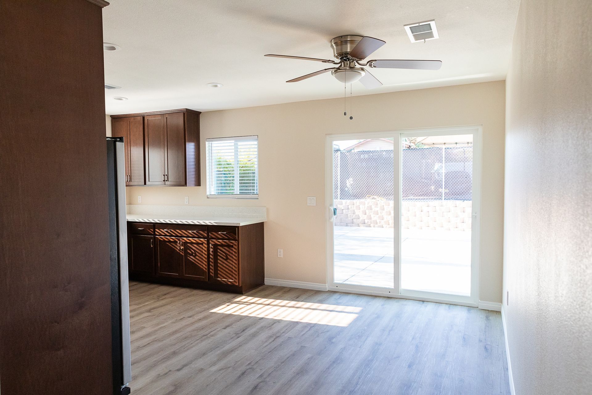 Empty living room with kitchen nook, ceiling fan, and sliding glass doors to a patio.