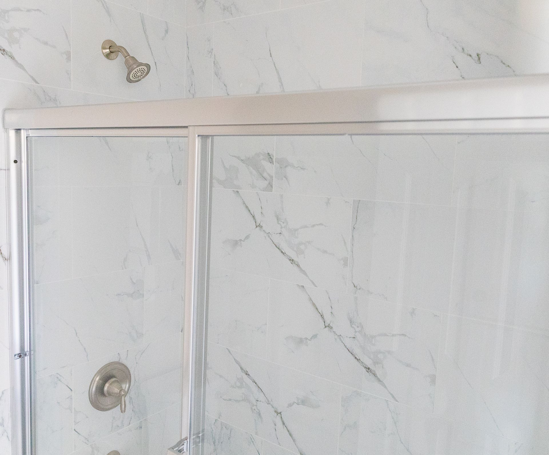 White shower door with chrome handle and marble-look tile wall