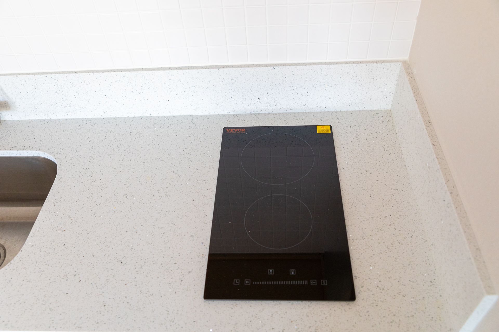 Black induction cooktop on a light countertop beside a stainless sink.