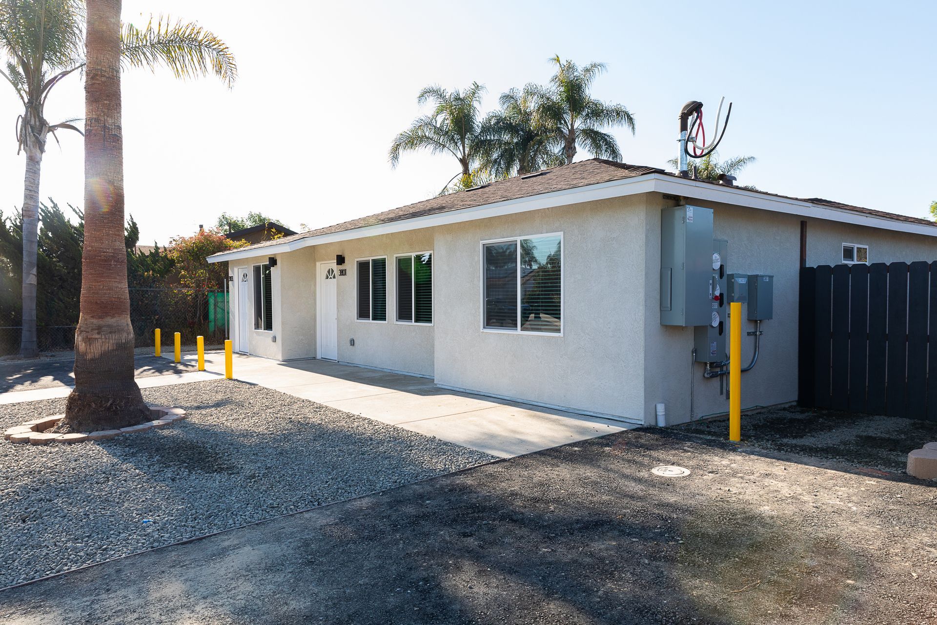 Single-story white house with palm trees, gravel driveway, and yellow utility poles in front