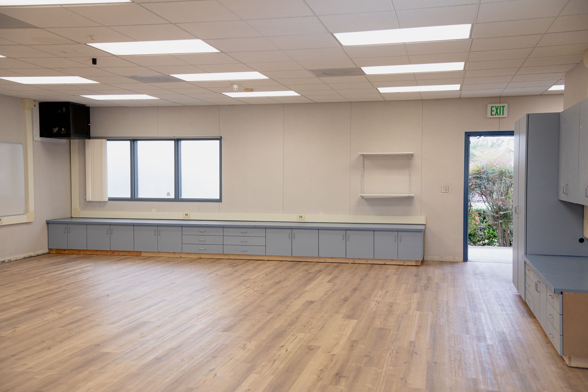 Empty room with wood floors, gray cabinets, fluorescent lights, and a windowed door to the outside.
