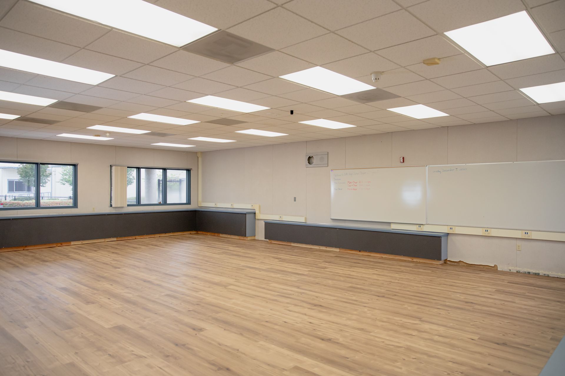 Empty classroom with wood floor, whiteboard, windows, and ceiling lights