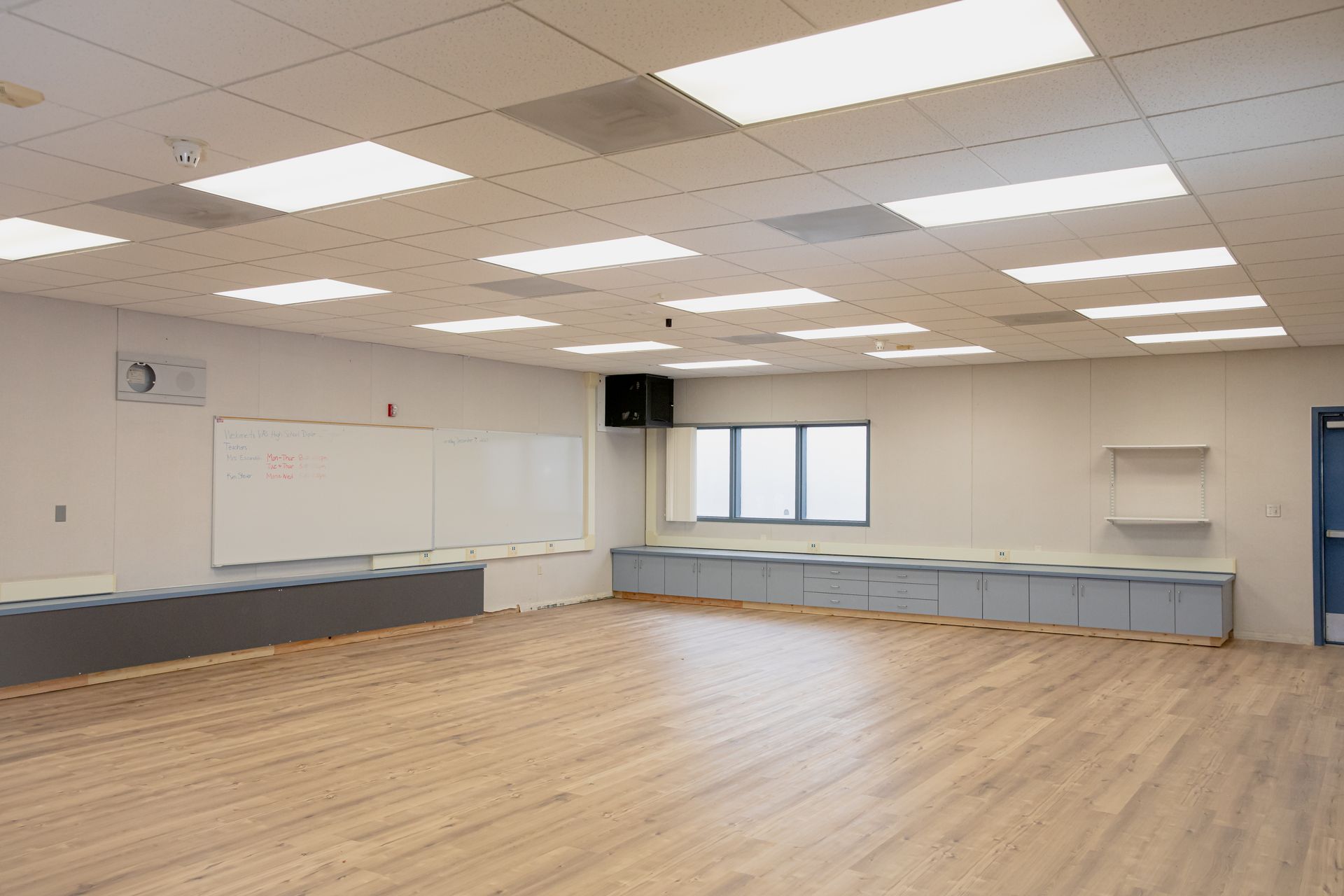 Empty classroom with wood floor, whiteboard, and fluorescent ceiling lights