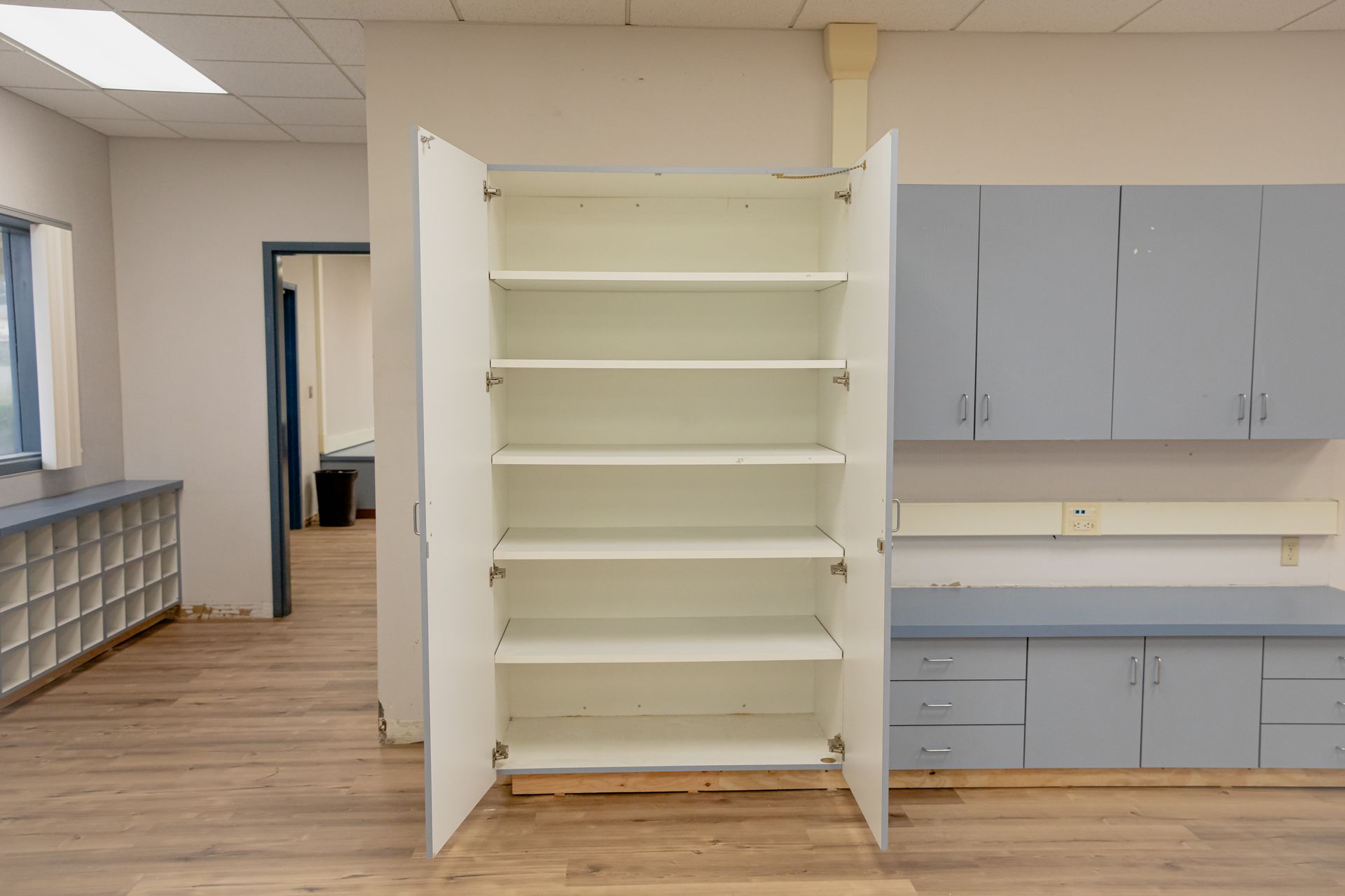 Empty white shelving unit in a room with gray cabinets and wood flooring