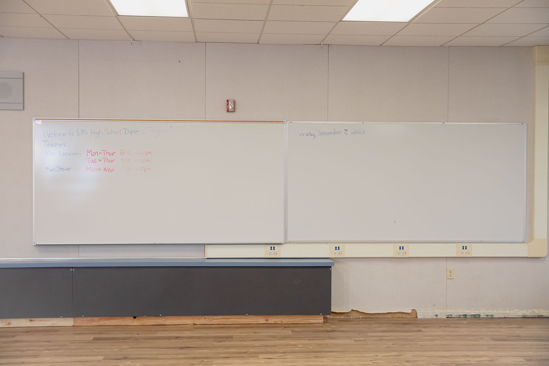 Empty classroom with two whiteboards, a gray wall, and a wooden floor.