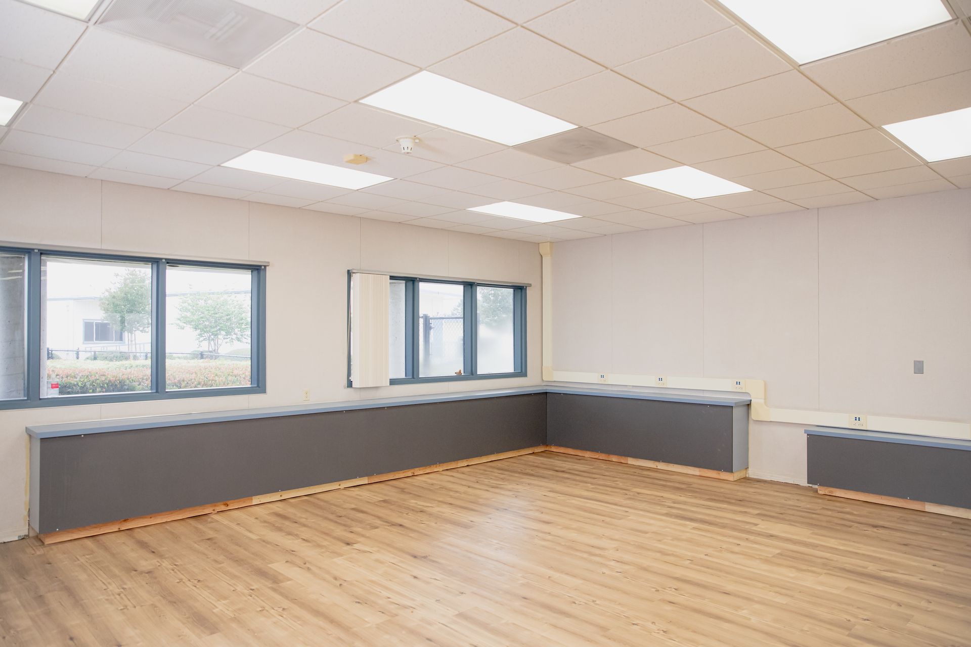 Empty modern office room with wood floor, gray walls, windows, and recessed ceiling lights