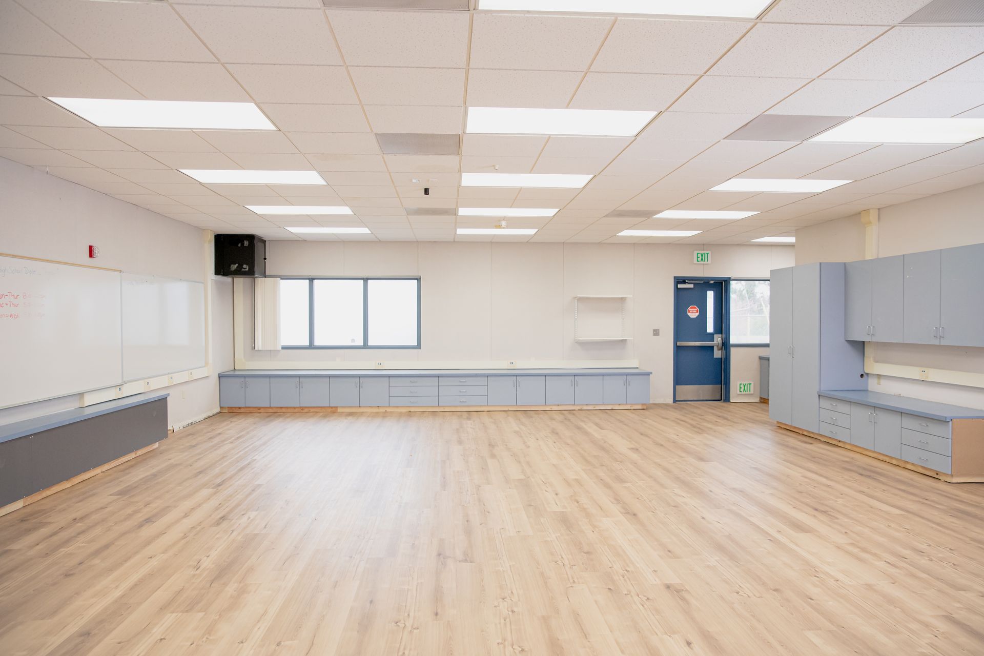 Empty bright classroom with wood floors, gray cabinets, and fluorescent ceiling lights