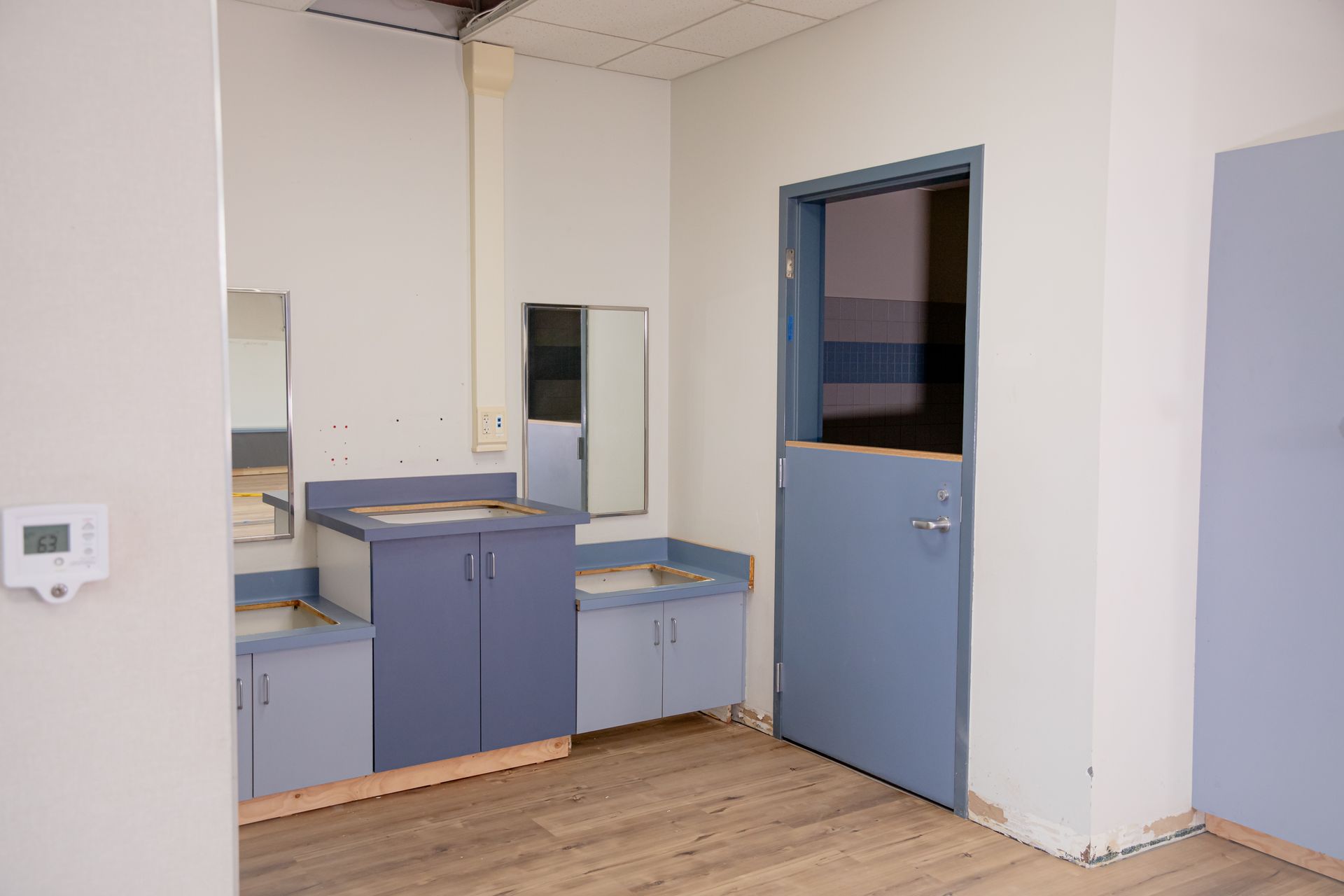 Small office sink area with blue cabinets, mirror, and open blue door