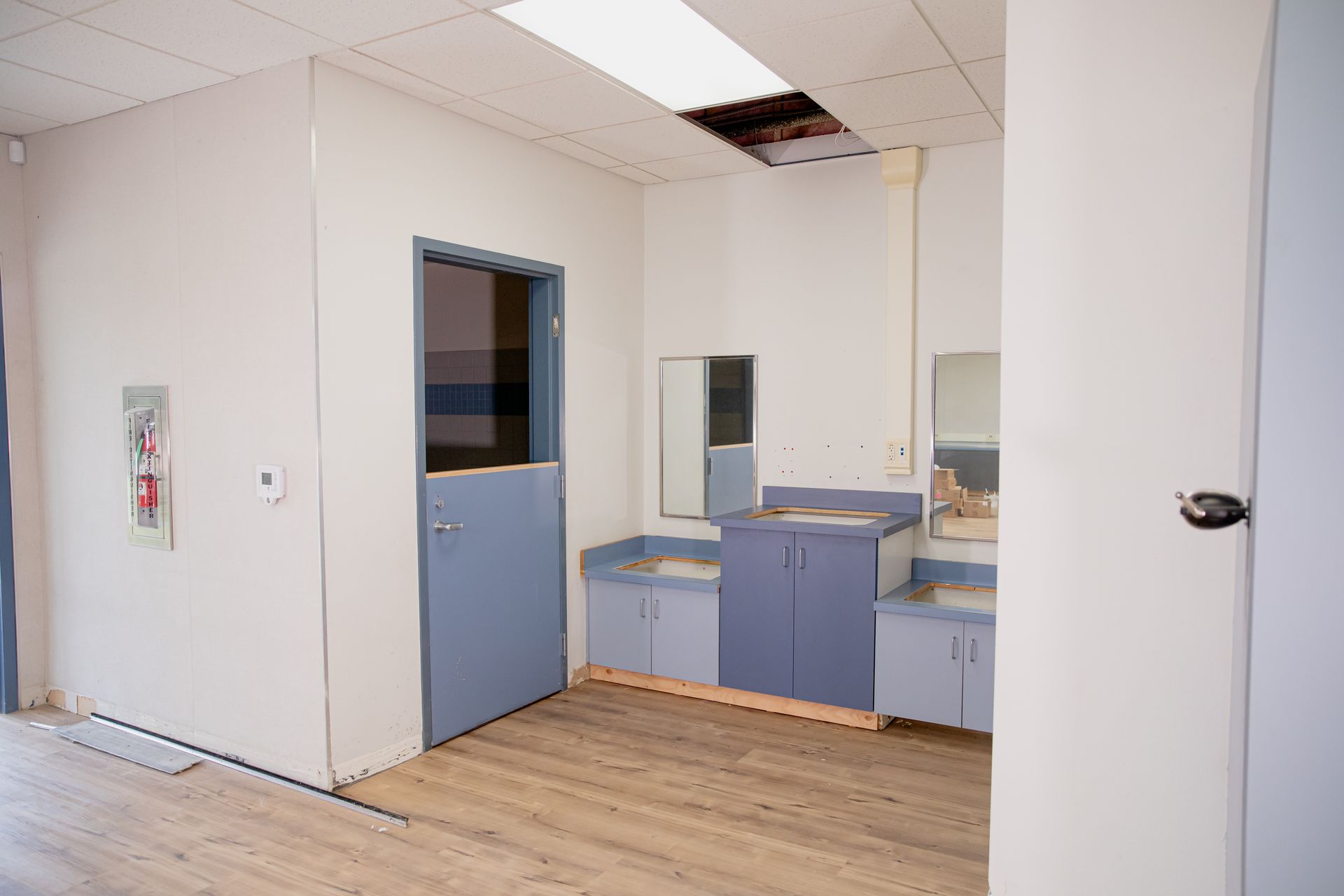 Small office kitchenette with blue cabinets, sink, and mirror in a partially tiled room