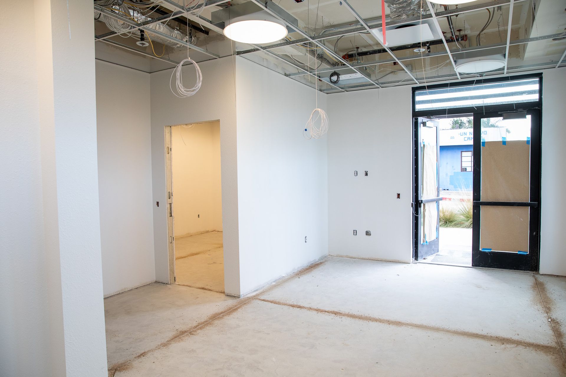Empty room under construction with exposed ceiling, white walls, and open doorway to daylight