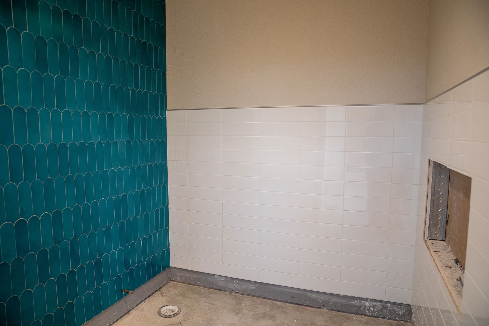 Empty bathroom under construction with teal and white tiled walls and unfinished floor