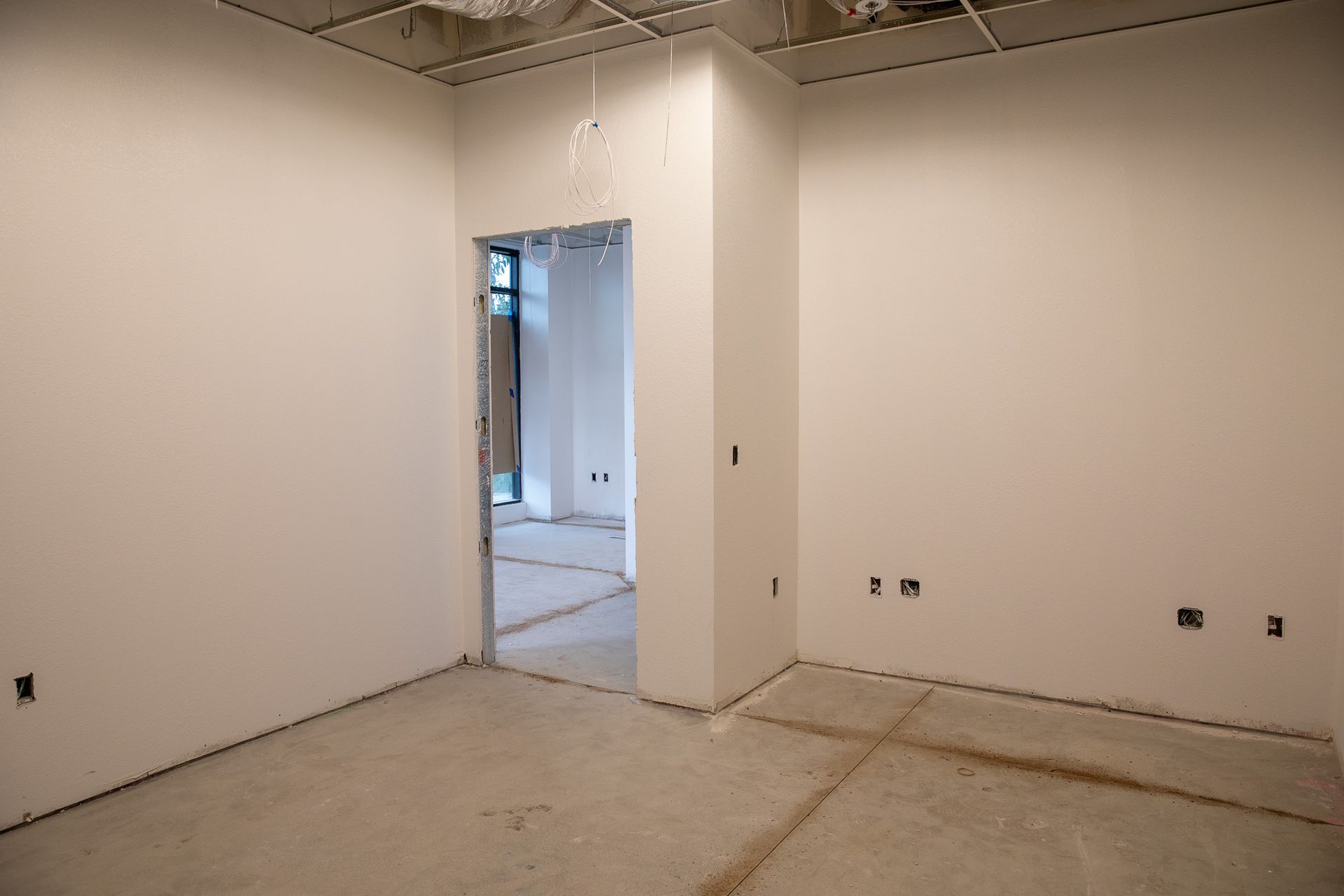 Empty unfinished room with white walls, exposed ceiling, and doorway opening to a hallway