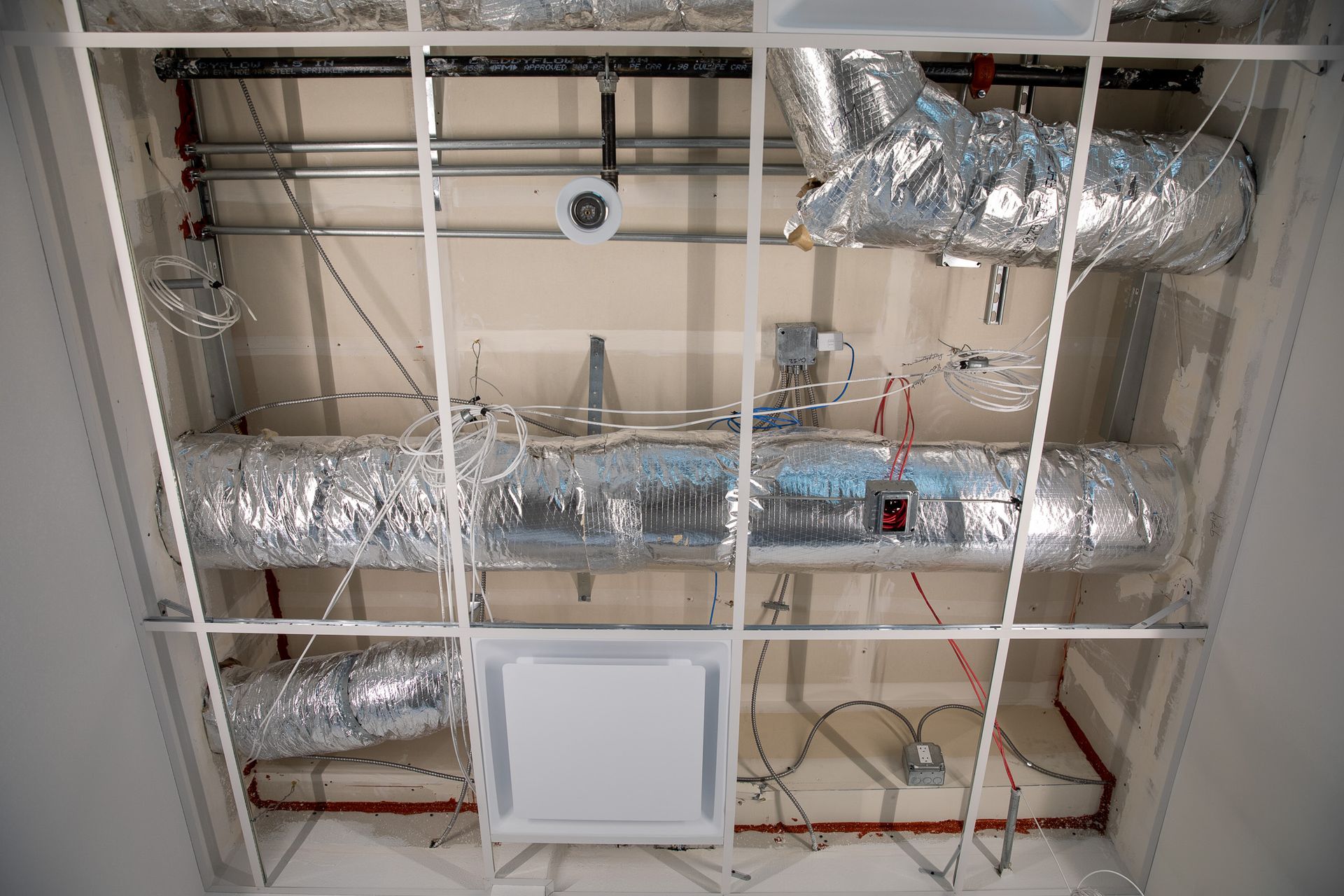 Exposed ceiling HVAC ductwork and pipes in a utility space, with insulation and a central access panel.