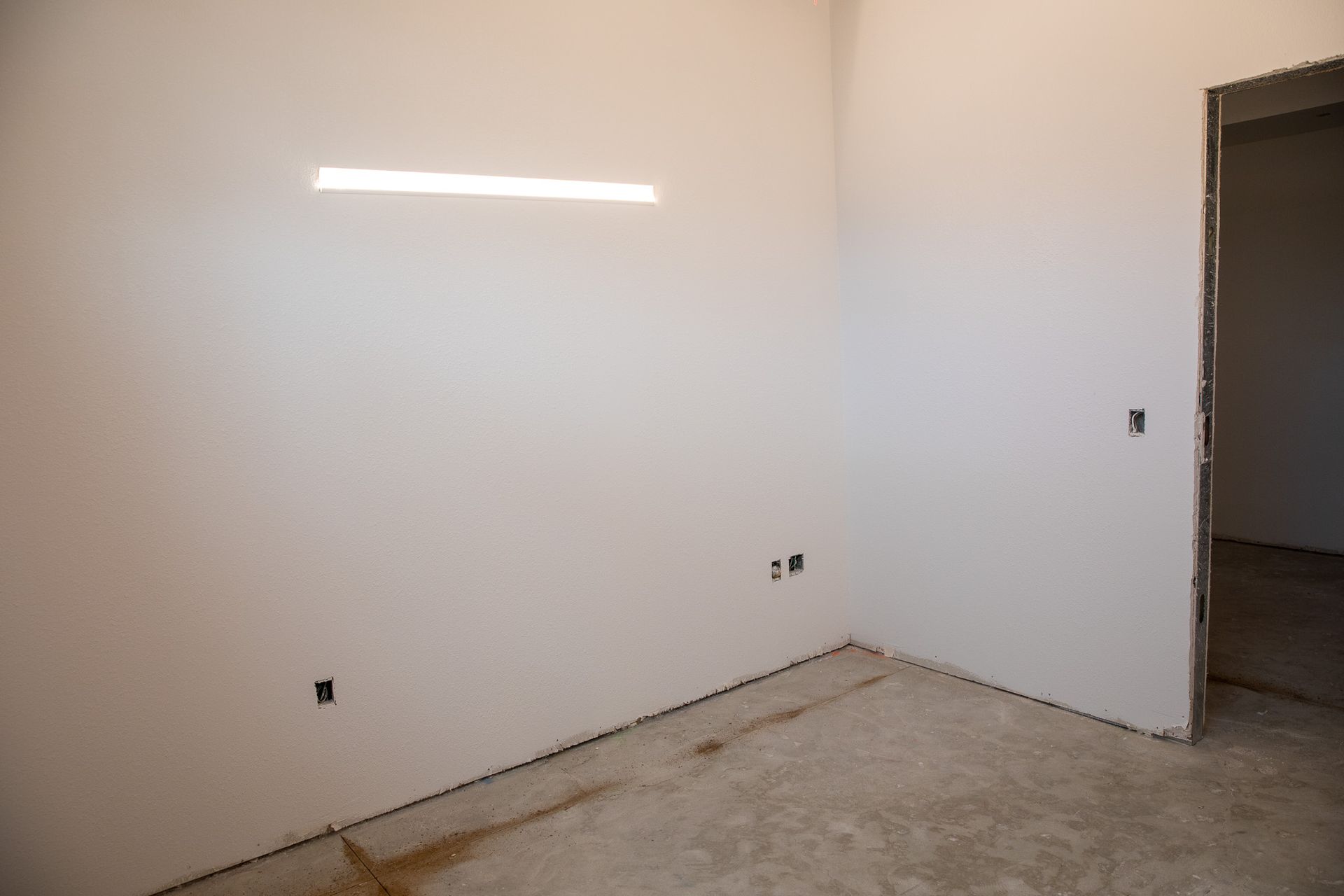 Empty white room with unfinished concrete floor and open doorway