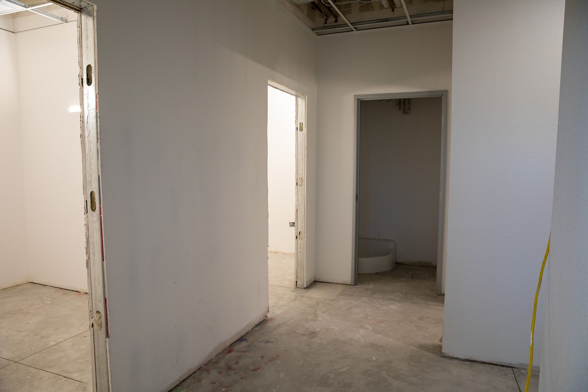 Empty unfinished hallway with white walls, doorways, and a concrete floor