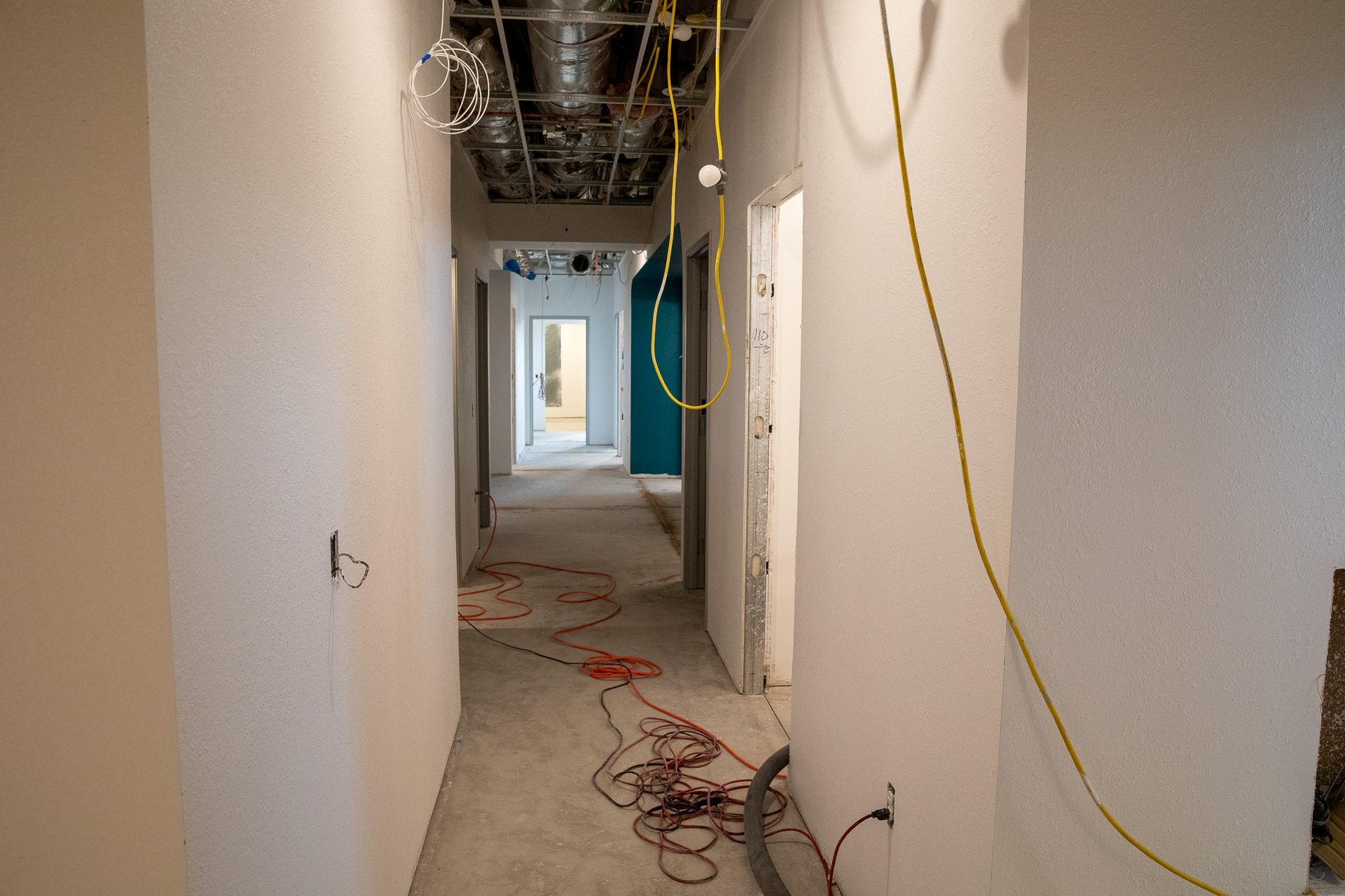 Unfinished hallway with exposed ceiling wiring and construction cables on the floor