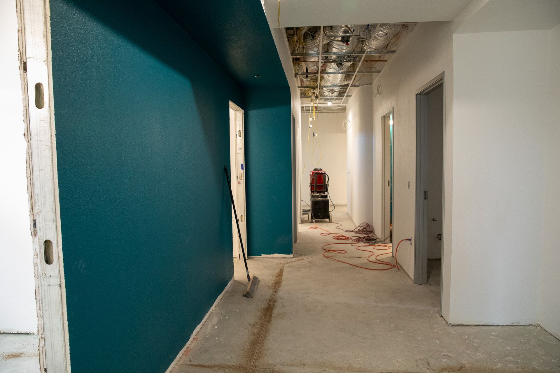 Empty hallway under construction with teal and white walls, exposed ceiling, and debris on the floor