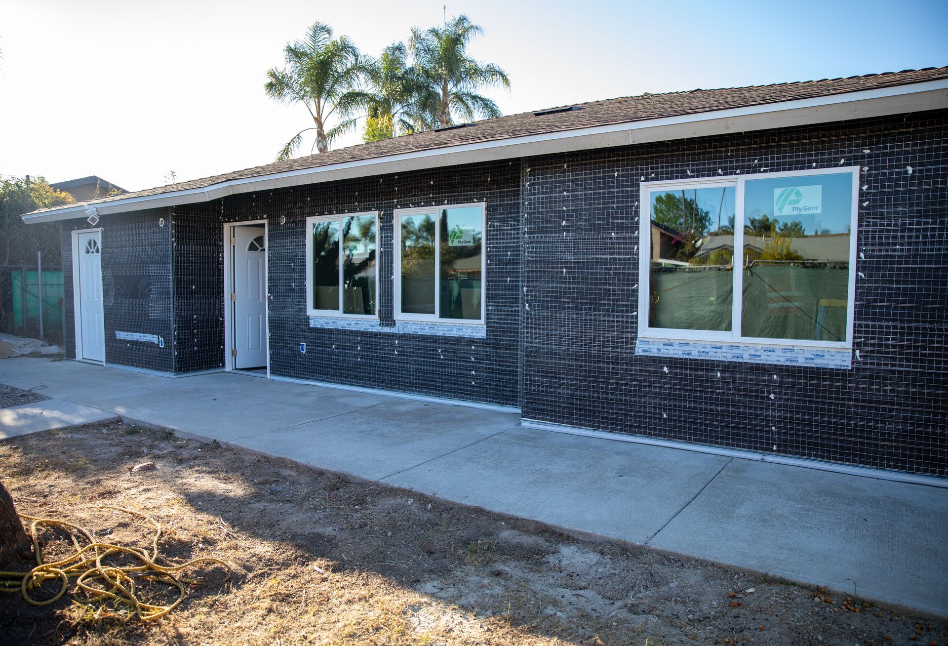 Single-story brick building exterior with windows, a sidewalk, and palm trees in the background